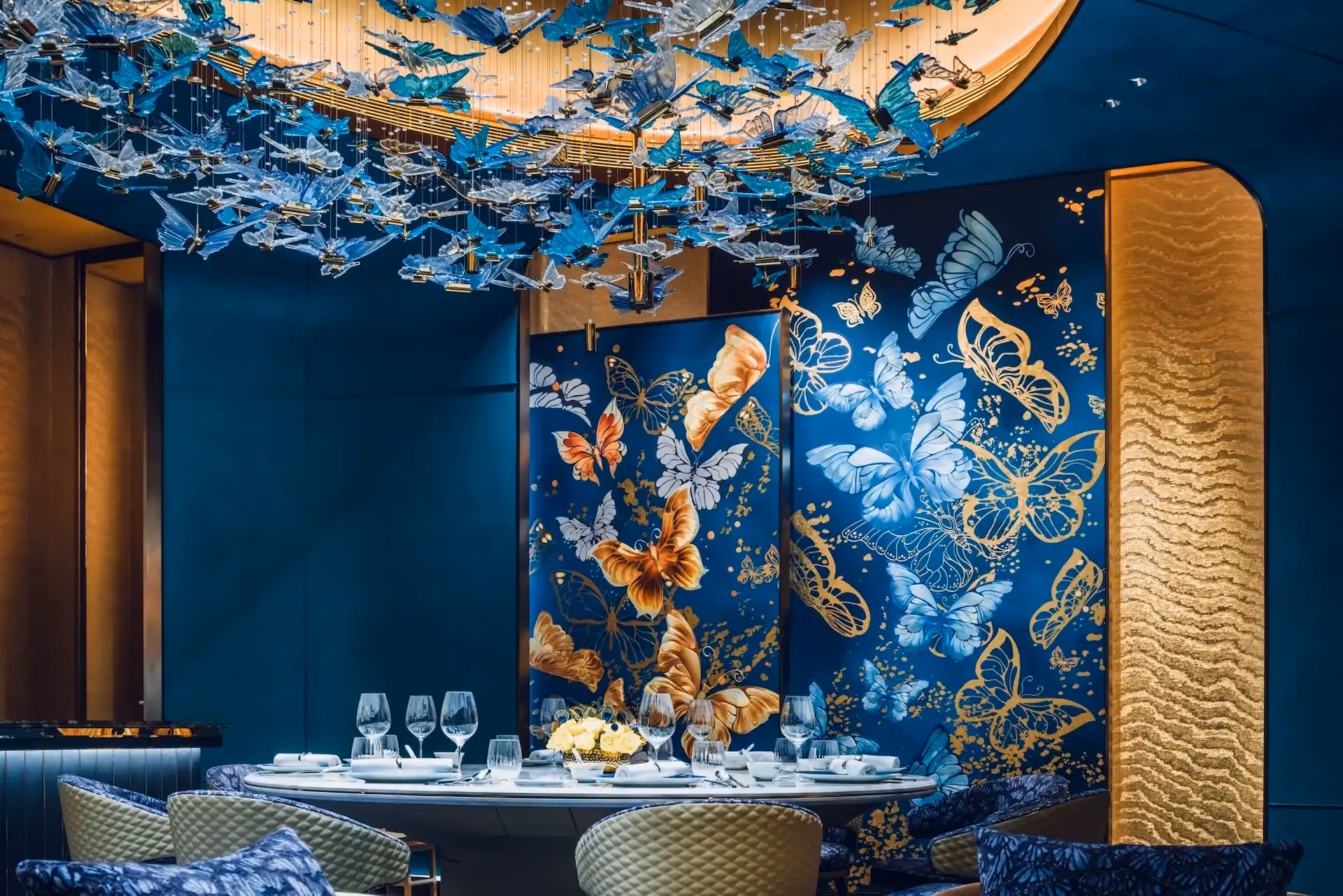Grand Imperial Court private dining detail at MGM Macao featuring bespoke butterfly wall panels in blue and gold tones circular dining table crystal glassware and suspended butterfly chandelier within a luxury Chinese restaurant interior design