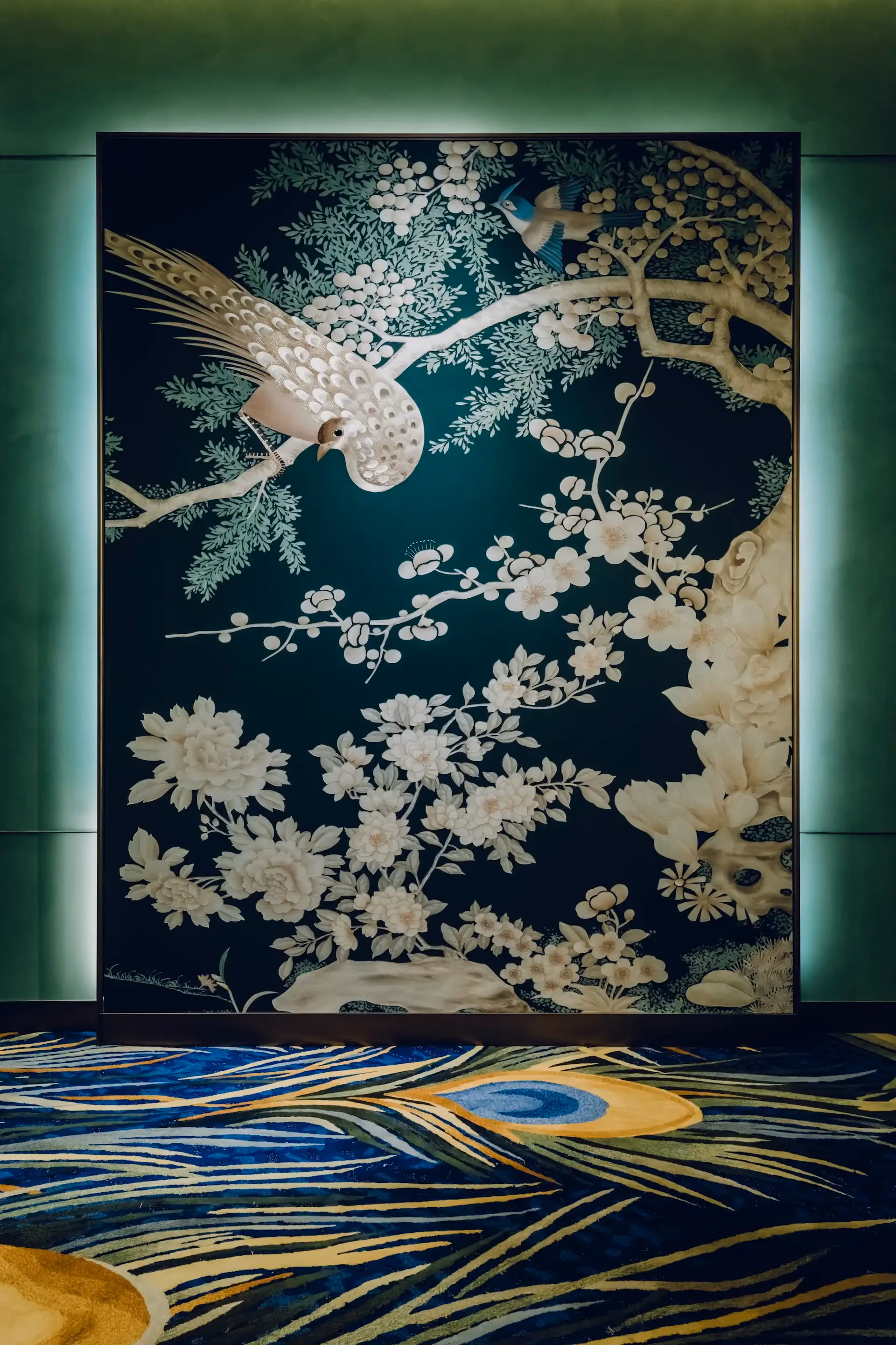 Grand Imperial Court Tapestry Of Feathers entrance artwork at MGM Macao featuring large scale wall mural with bird and floral motifs set against deep teal background with illuminated perimeter detail and bespoke patterned carpet within a luxury Chinese restaurant interior design