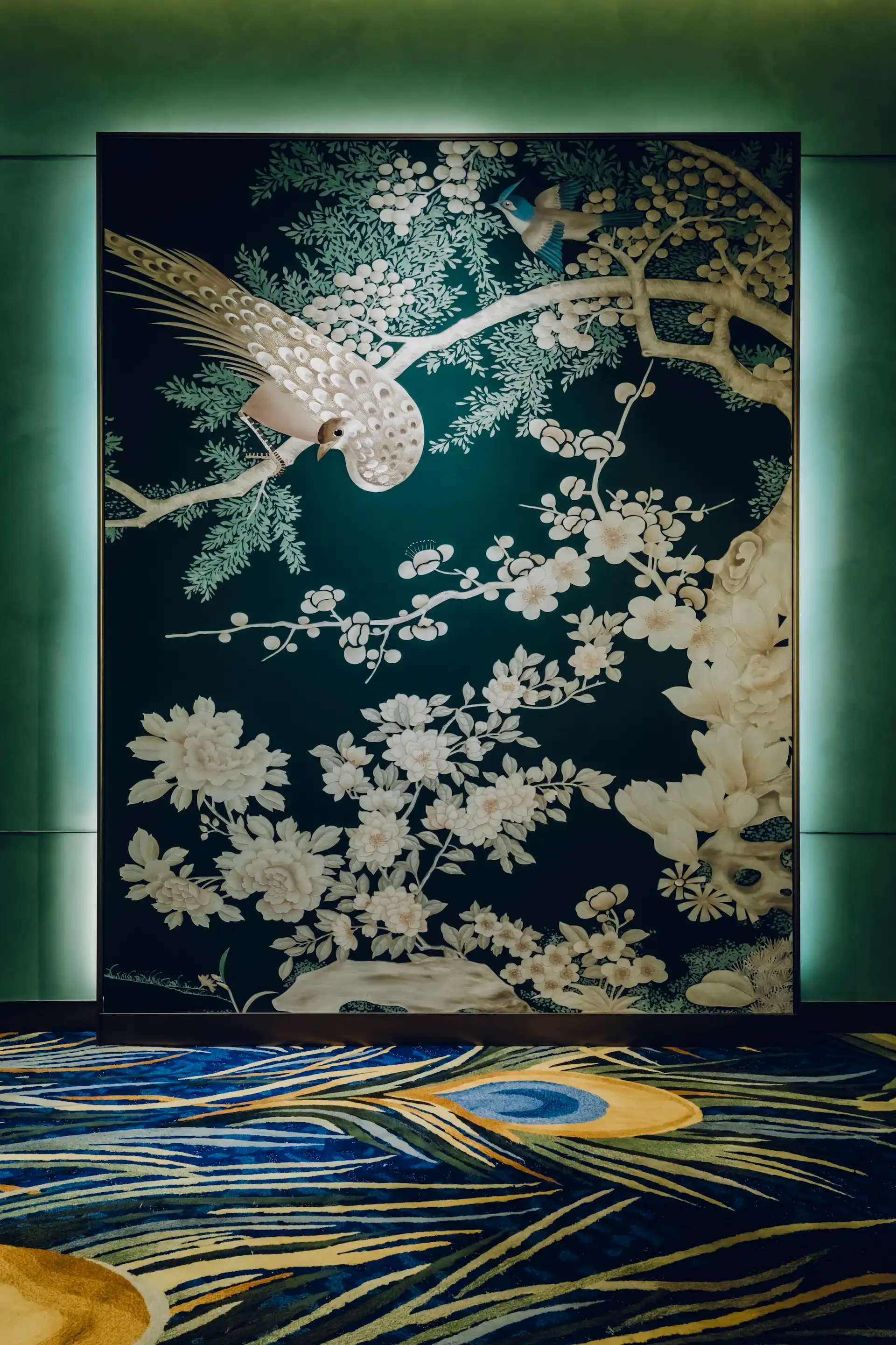 Grand Imperial Court Tapestry Of Feathers entrance artwork at MGM Macao featuring large scale wall mural with bird and floral motifs set against deep teal background with illuminated perimeter detail and bespoke patterned carpet within a luxury Chinese restaurant interior design