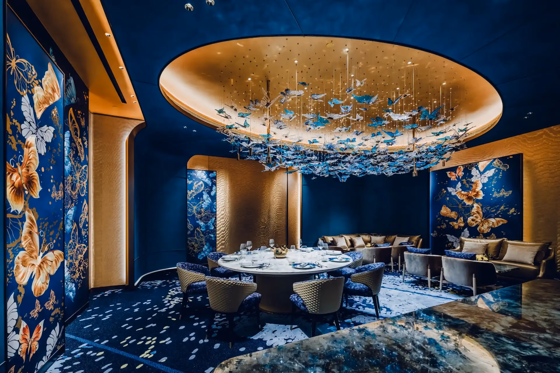 Grand Imperial Court Tapestry Butterfly Wings private dining room at MGM Macao featuring circular dining table bespoke butterfly wall panels deep blue interior finishes curved gold ceiling detail and suspended butterfly chandelier installation within a luxury Chinese restaurant design