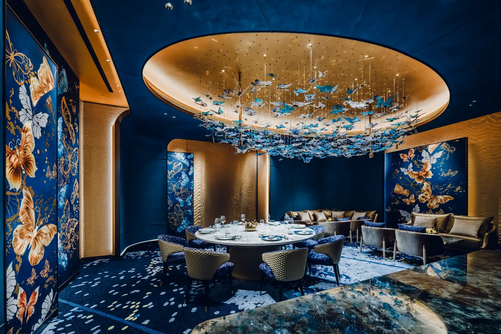 Grand Imperial Court Tapestry Butterfly Wings private dining room at MGM Macao featuring circular dining table bespoke butterfly wall panels deep blue interior finishes curved gold ceiling detail and suspended butterfly chandelier installation within a luxury Chinese restaurant design