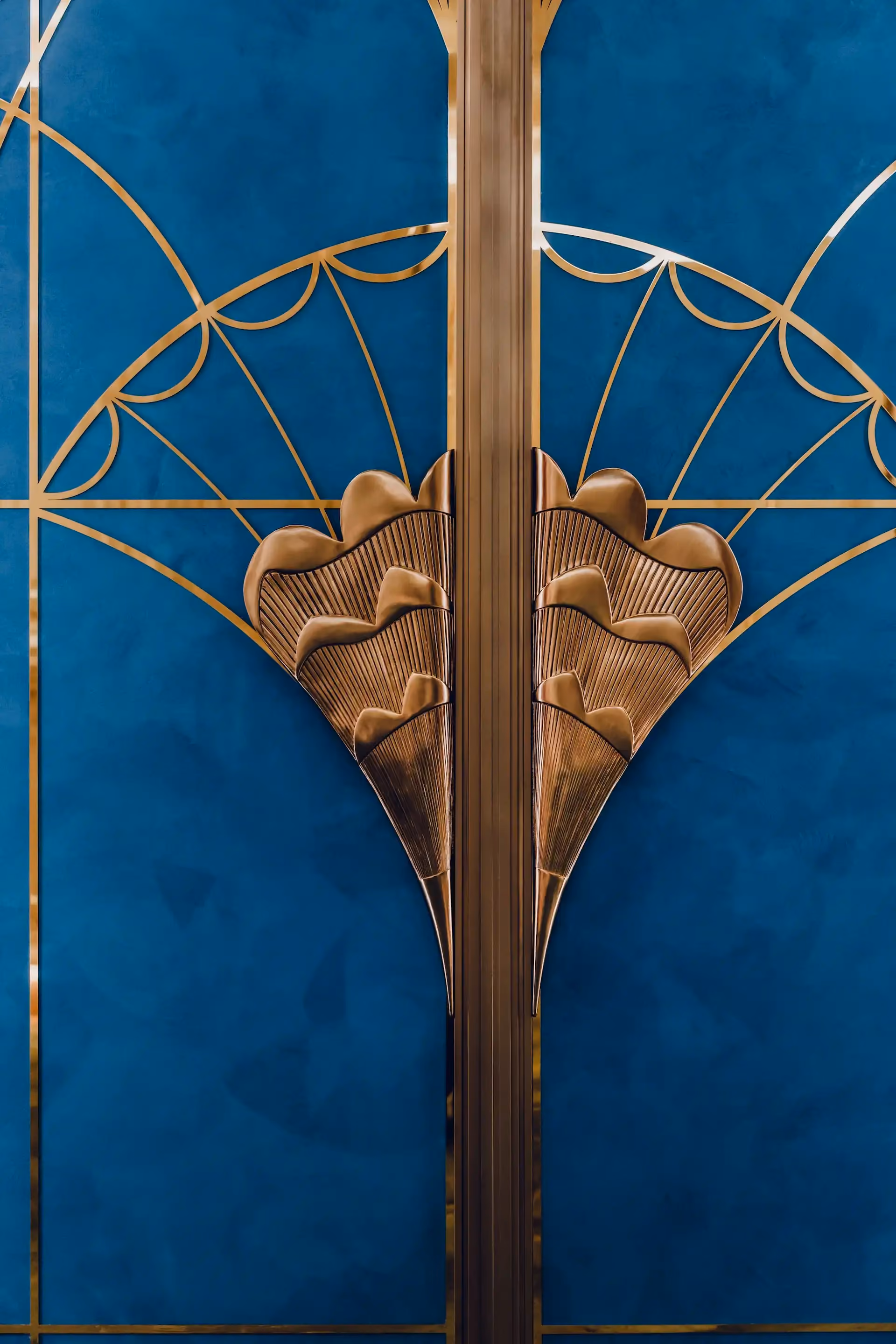 Close up of sculptural brass door handle inspired by tapestry butterfly wings at Grand Imperial Court MGM Macao featuring blue lacquer panel background and geometric brass inlay within a luxury Chinese restaurant private dining room interior
