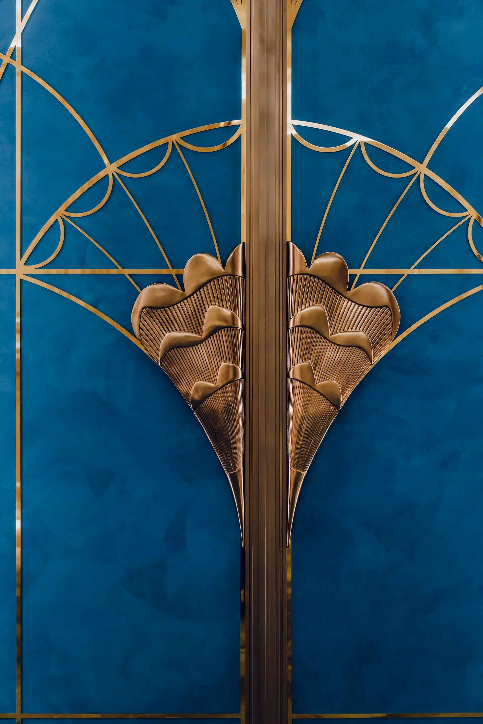 Close up of sculptural brass door handle inspired by tapestry butterfly wings at Grand Imperial Court MGM Macao featuring blue lacquer panel background and geometric brass inlay within a luxury Chinese restaurant private dining room interior