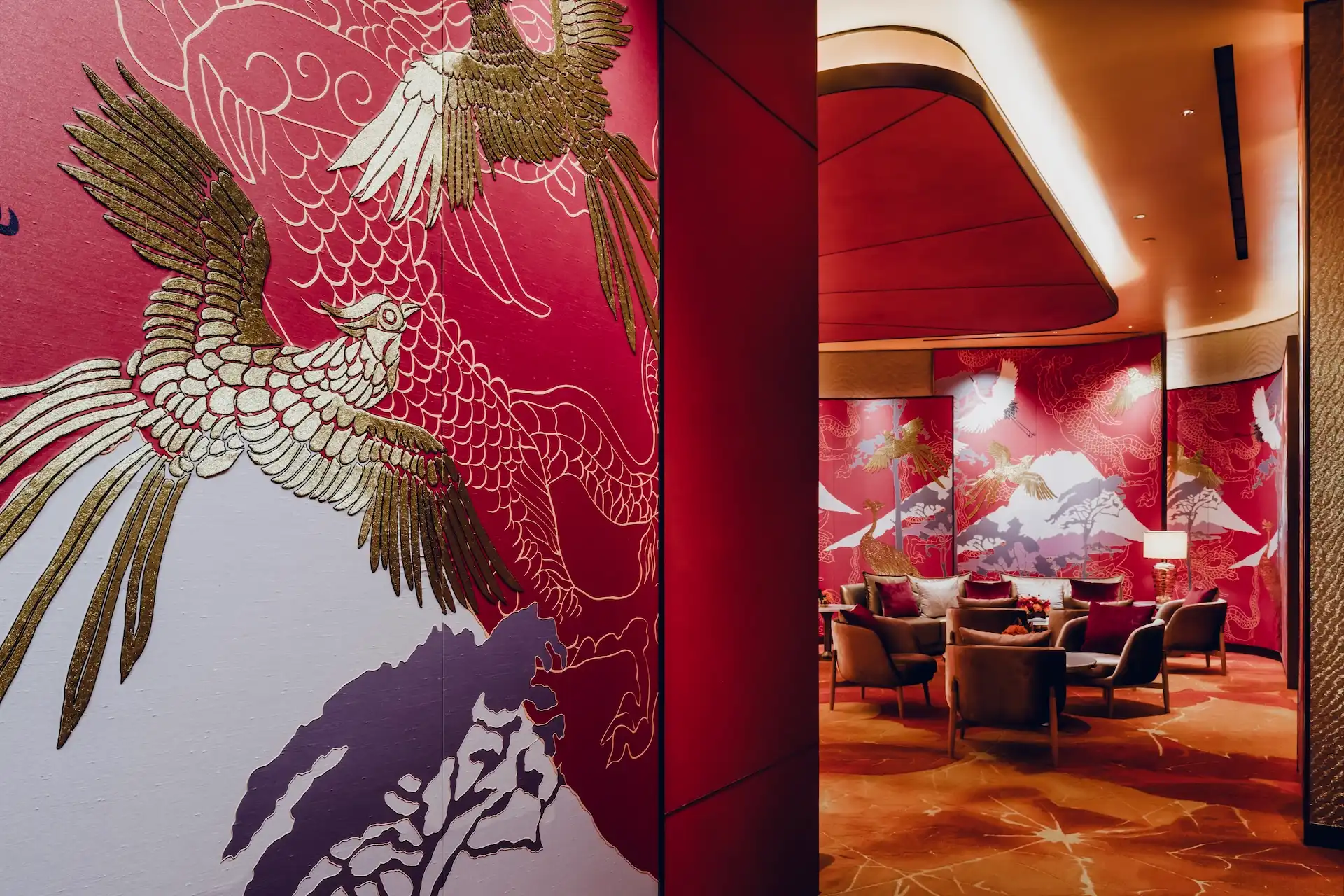 Grand Imperial Court Tapestry Of Parchment private lounge at MGM Macao featuring red lacquered wall panels with gold phoenix artwork mountain motif detailing curved ceiling recess bespoke patterned carpet and intimate lounge seating within a luxury Chinese restaurant interior design