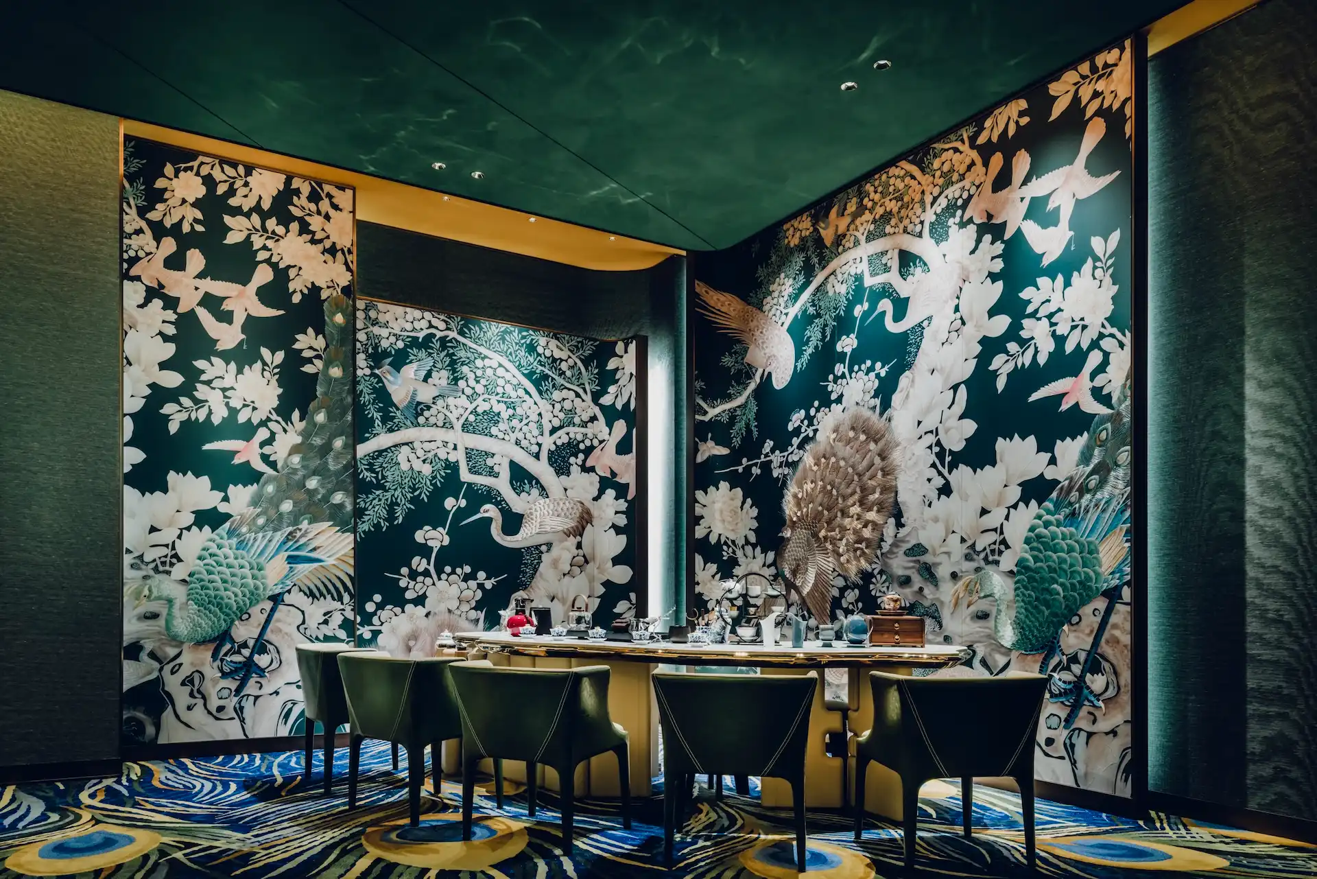 Grand Imperial Court Tapestry Of Feathers wall mural detail at MGM Macao featuring large scale peacock and crane artwork with floral motifs green lacquered walls bespoke carpet with feather pattern and private dining table setting within a luxury Chinese restaurant interior design