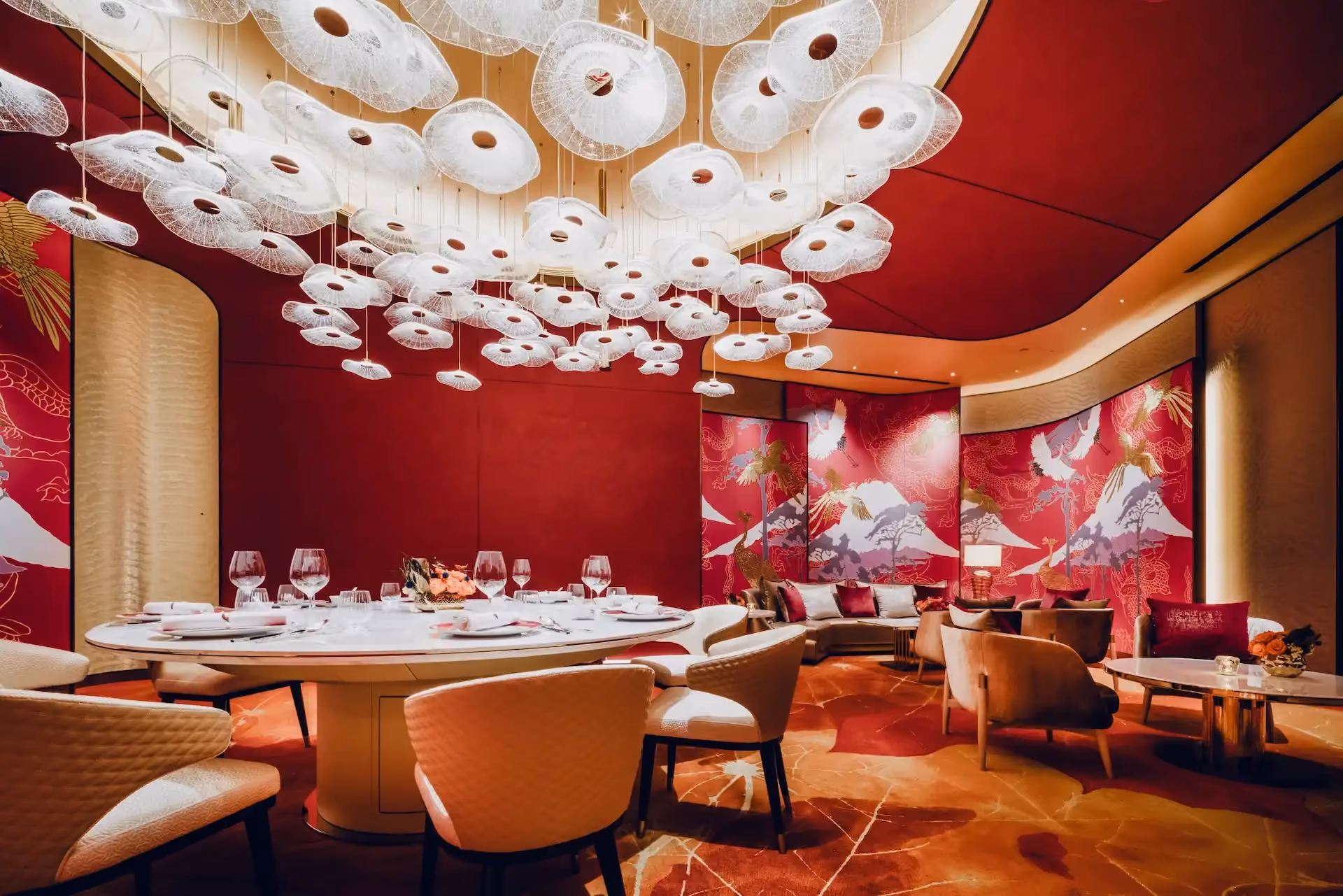 Grand Imperial Court Tapestry Of Parchment dining room at MGM Macao featuring illuminated red lacquer wall murals with gold phoenix and mountain motifs sculptural white pendant light installation round marble banquet table upholstered dining chairs bespoke patterned flooring and lounge seating within a luxury Chinese restaurant interior design