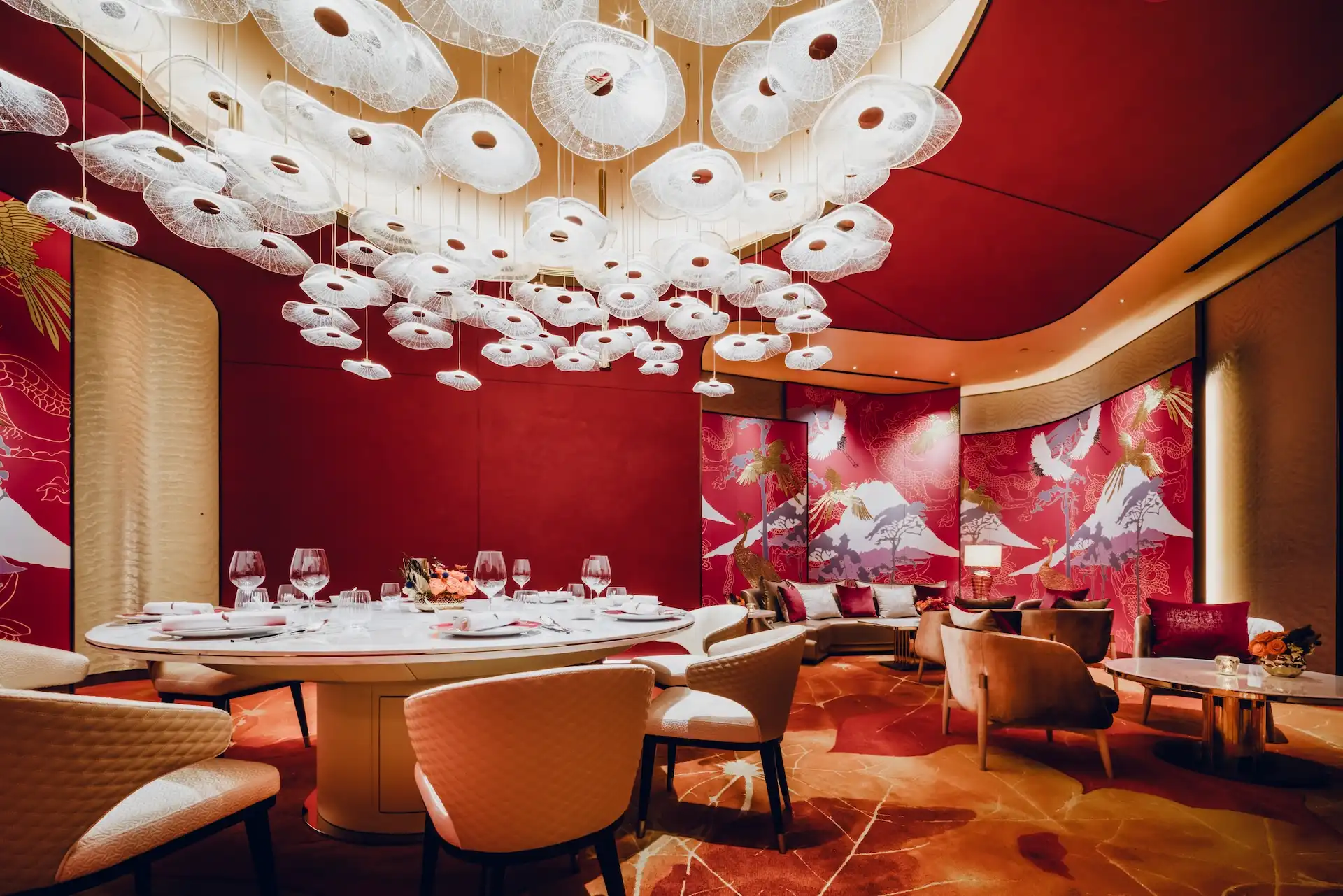 Grand Imperial Court Tapestry Of Parchment dining room at MGM Macao featuring illuminated red lacquer wall murals with gold phoenix and mountain motifs sculptural white pendant light installation round marble banquet table upholstered dining chairs bespoke patterned flooring and lounge seating within a luxury Chinese restaurant interior design