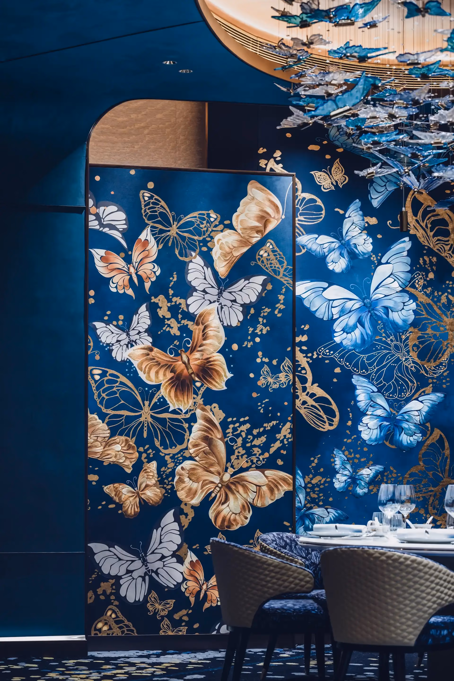 Grand Imperial Court butterfly wall panel detail at MGM Macao featuring blue and gold bespoke artwork layered butterfly motifs curved architectural opening and private dining table setting within a luxury Chinese restaurant interior design