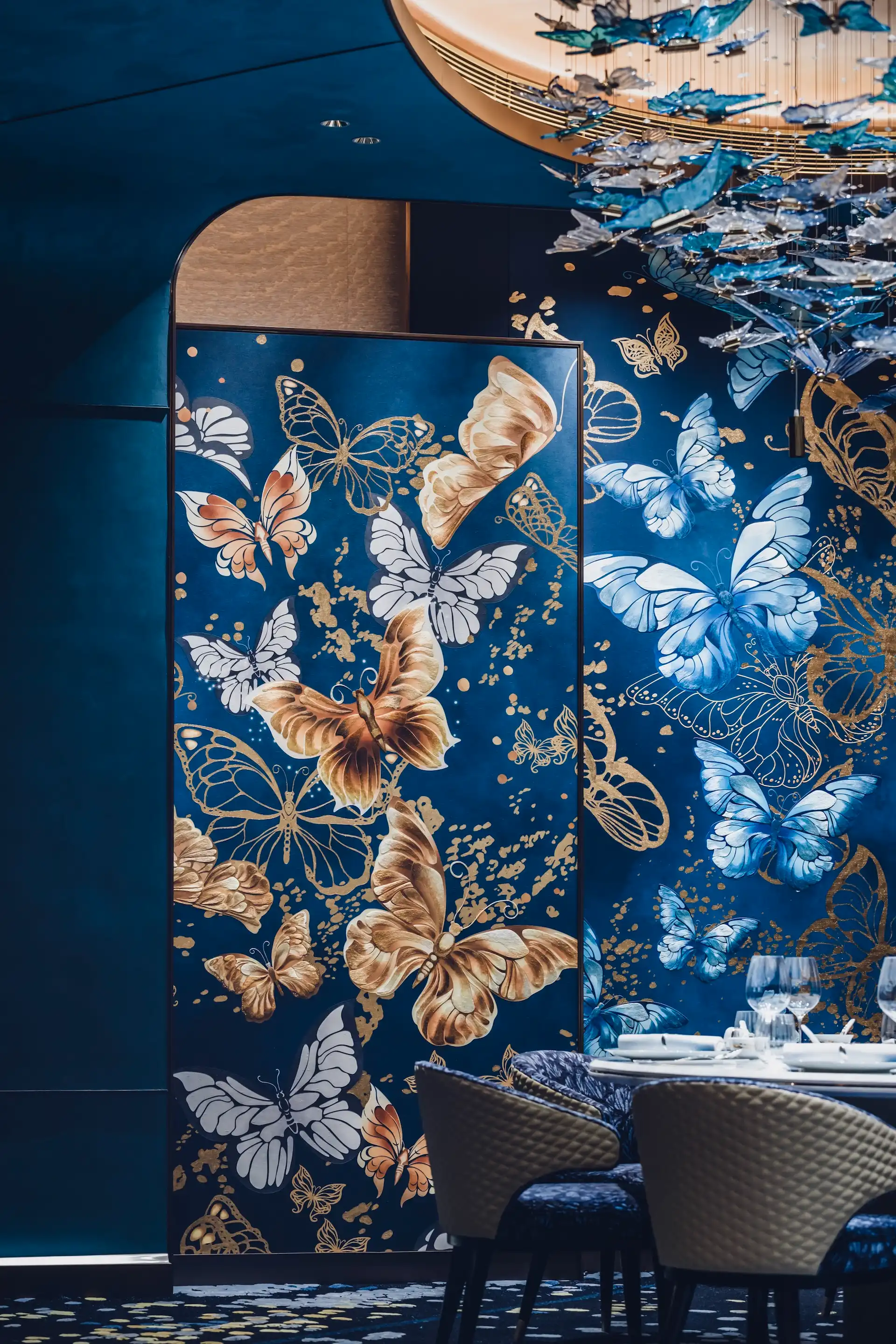 Grand Imperial Court butterfly wall panel detail at MGM Macao featuring blue and gold bespoke artwork layered butterfly motifs curved architectural opening and private dining table setting within a luxury Chinese restaurant interior design