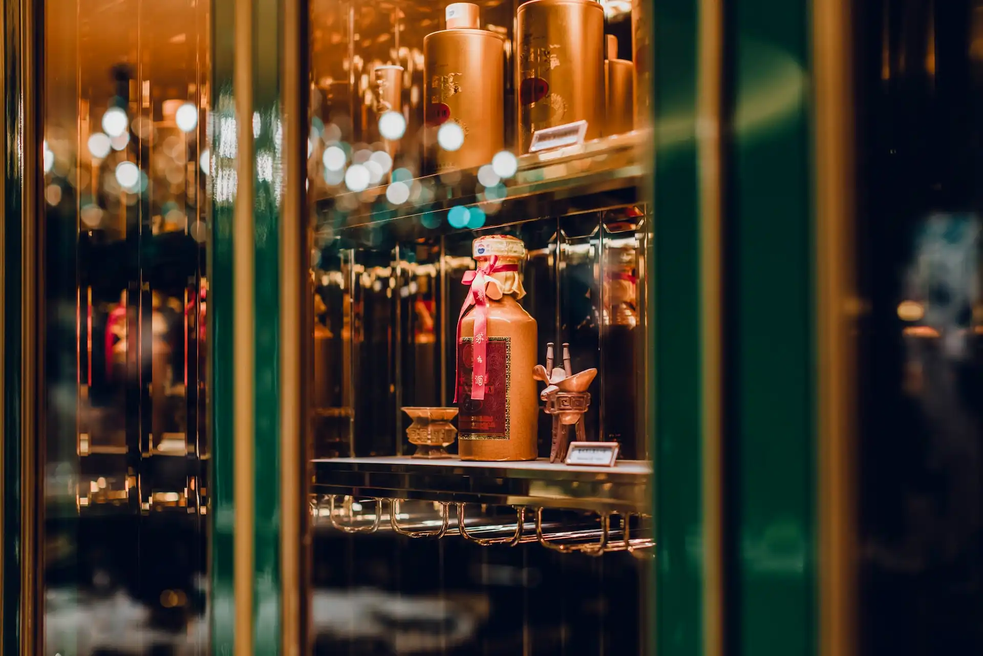 Grand Imperial Court Moutai display cabinet detail at MGM Macao featuring illuminated glass shelving lacquered green framing reflective mirrored panels and premium Chinese liquor presentation within a luxury restaurant interior design