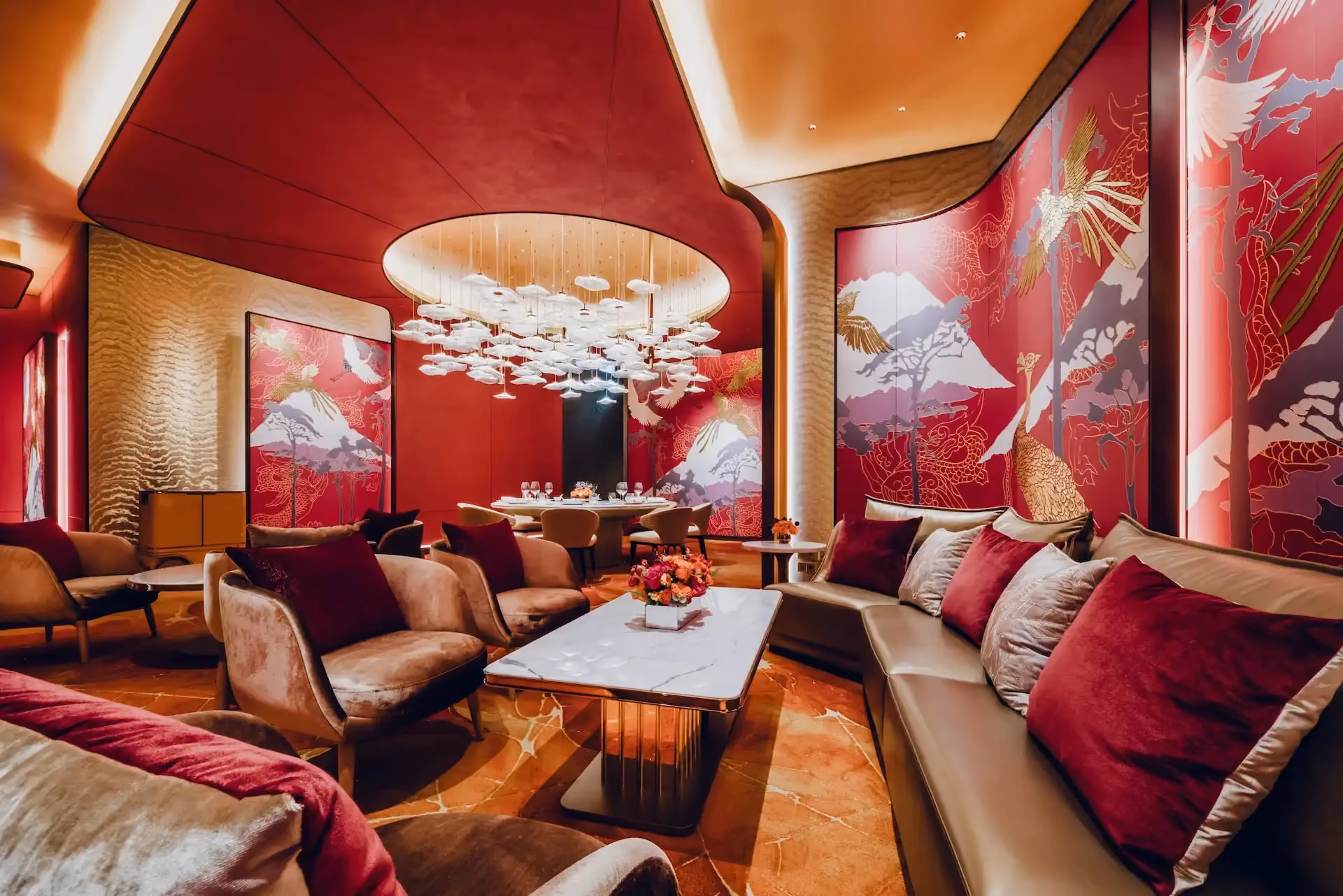 Grand Imperial Court Tapestry Of Parchment lounge interior at MGM Macao featuring red lacquered wall murals with gold phoenix and mountain motifs curved ceiling recess sculptural pendant lighting marble coffee table plush lounge seating and bespoke patterned flooring within a luxury Chinese restaurant interior design