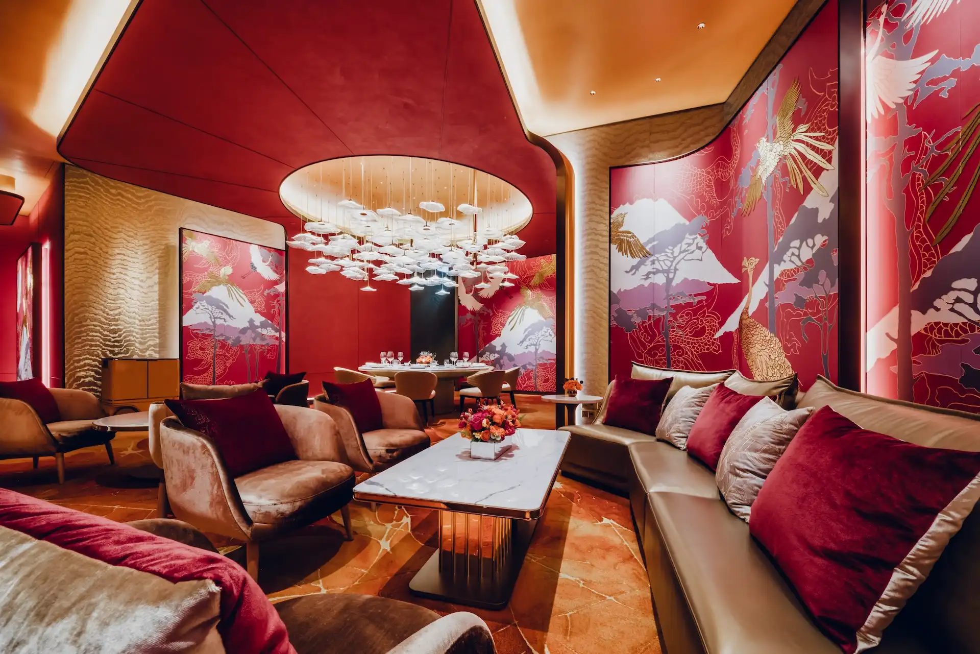 Grand Imperial Court Tapestry Of Parchment lounge interior at MGM Macao featuring red lacquered wall murals with gold phoenix and mountain motifs curved ceiling recess sculptural pendant lighting marble coffee table plush lounge seating and bespoke patterned flooring within a luxury Chinese restaurant interior design