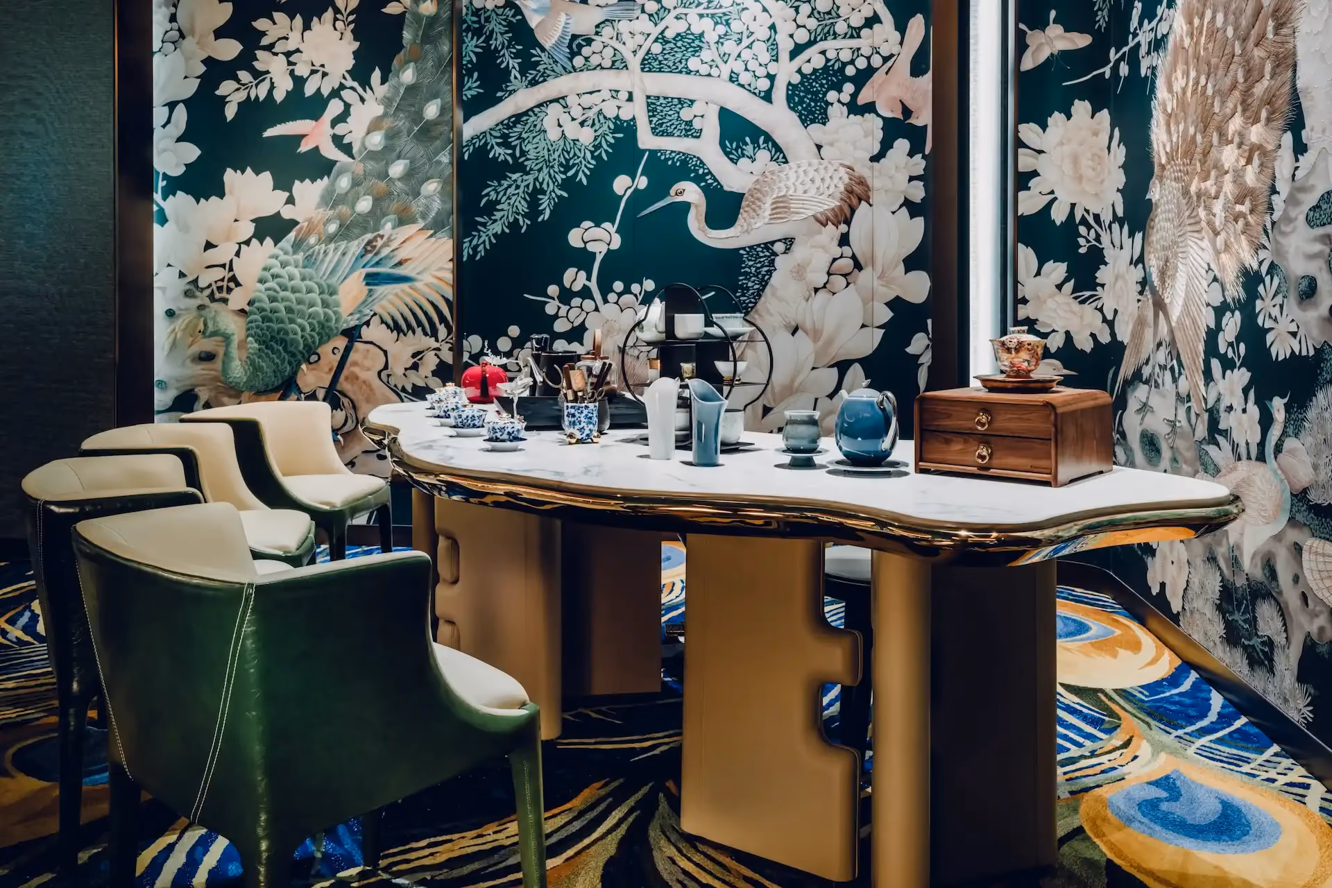 Grand Imperial Court tea ceremony table within Tapestry Of Feathers private dining room at MGM Macao featuring sculpted marble tabletop brass base detailing green leather dining chairs bespoke peacock and crane wall murals and custom feather patterned carpet in a luxury Chinese restaurant interior design