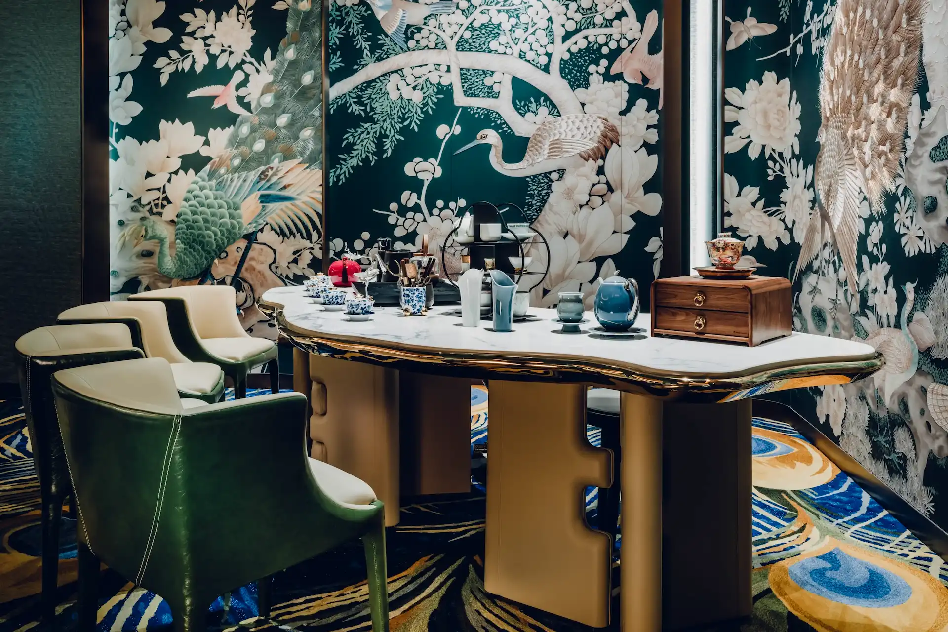 Grand Imperial Court tea ceremony table within Tapestry Of Feathers private dining room at MGM Macao featuring sculpted marble tabletop brass base detailing green leather dining chairs bespoke peacock and crane wall murals and custom feather patterned carpet in a luxury Chinese restaurant interior design
