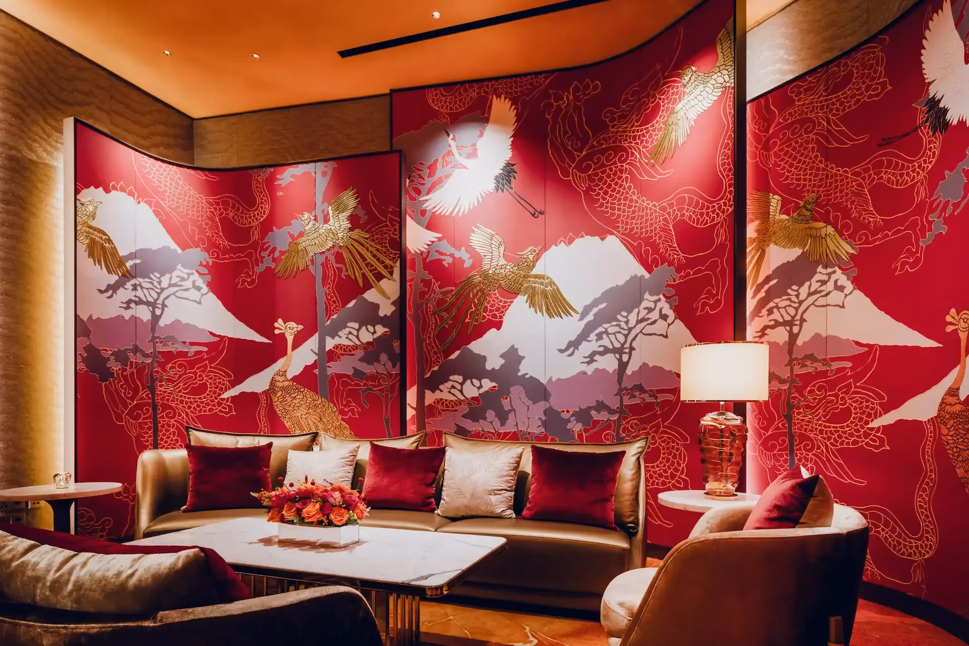 Grand Imperial Court Tapestry Of Parchment lounge detail at MGM Macao featuring red lacquer wall panels with gold phoenix and mountain artwork curved upholstered sofa marble coffee table decorative table lamp and bespoke patterned flooring within a luxury Chinese restaurant interior design