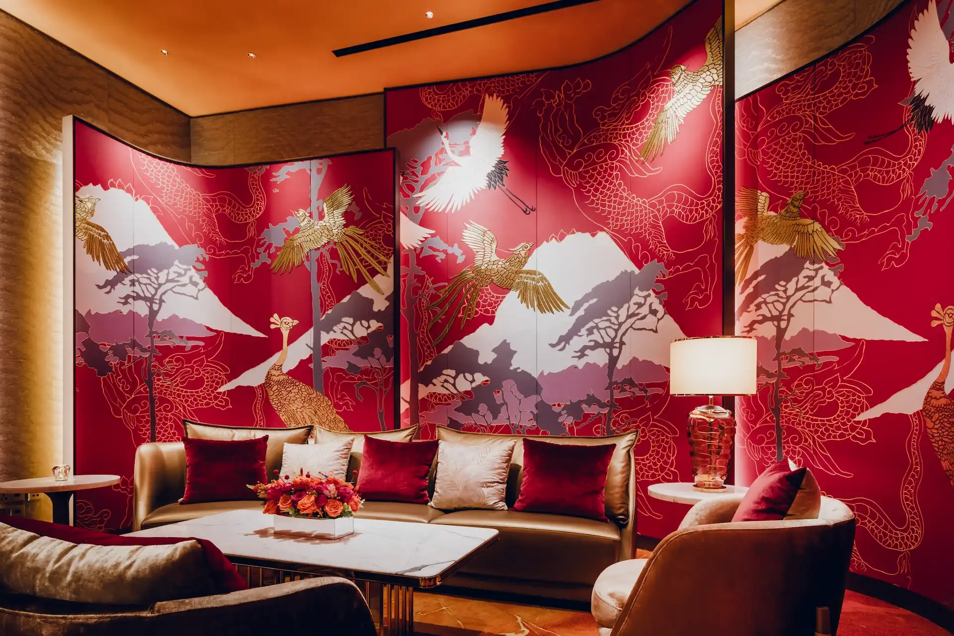 Grand Imperial Court Tapestry Of Parchment lounge detail at MGM Macao featuring red lacquer wall panels with gold phoenix and mountain artwork curved upholstered sofa marble coffee table decorative table lamp and bespoke patterned flooring within a luxury Chinese restaurant interior design
