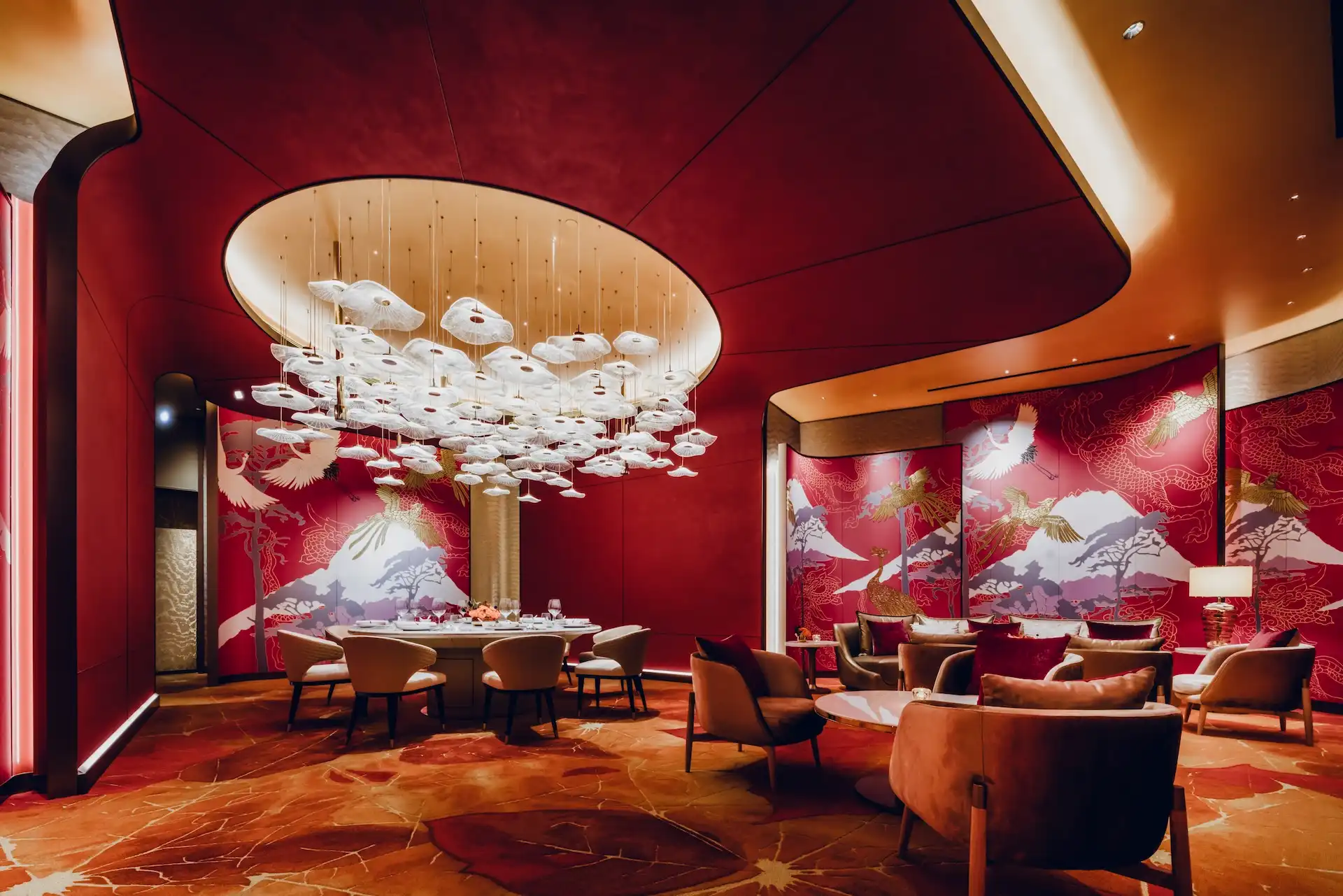Grand Imperial Court Tapestry Of Parchment private dining interior at MGM Macao featuring illuminated red lacquer wall murals with gold phoenix and mountain motifs sculptural white pendant light installation curved ceiling recess round banquet table upholstered dining chairs lounge seating and bespoke patterned flooring within a luxury Chinese restaurant design