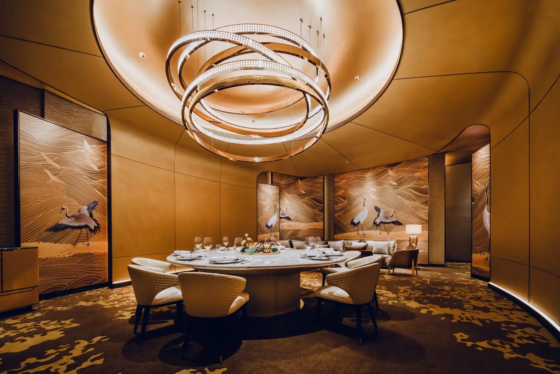 Grand Imperial Court private dining room at MGM Macao featuring sculptural circular chandelier suspended within recessed ceiling, round marble dining table with upholstered chairs and gold crane mural panels, defining a refined luxury Chinese restaurant interior design experience