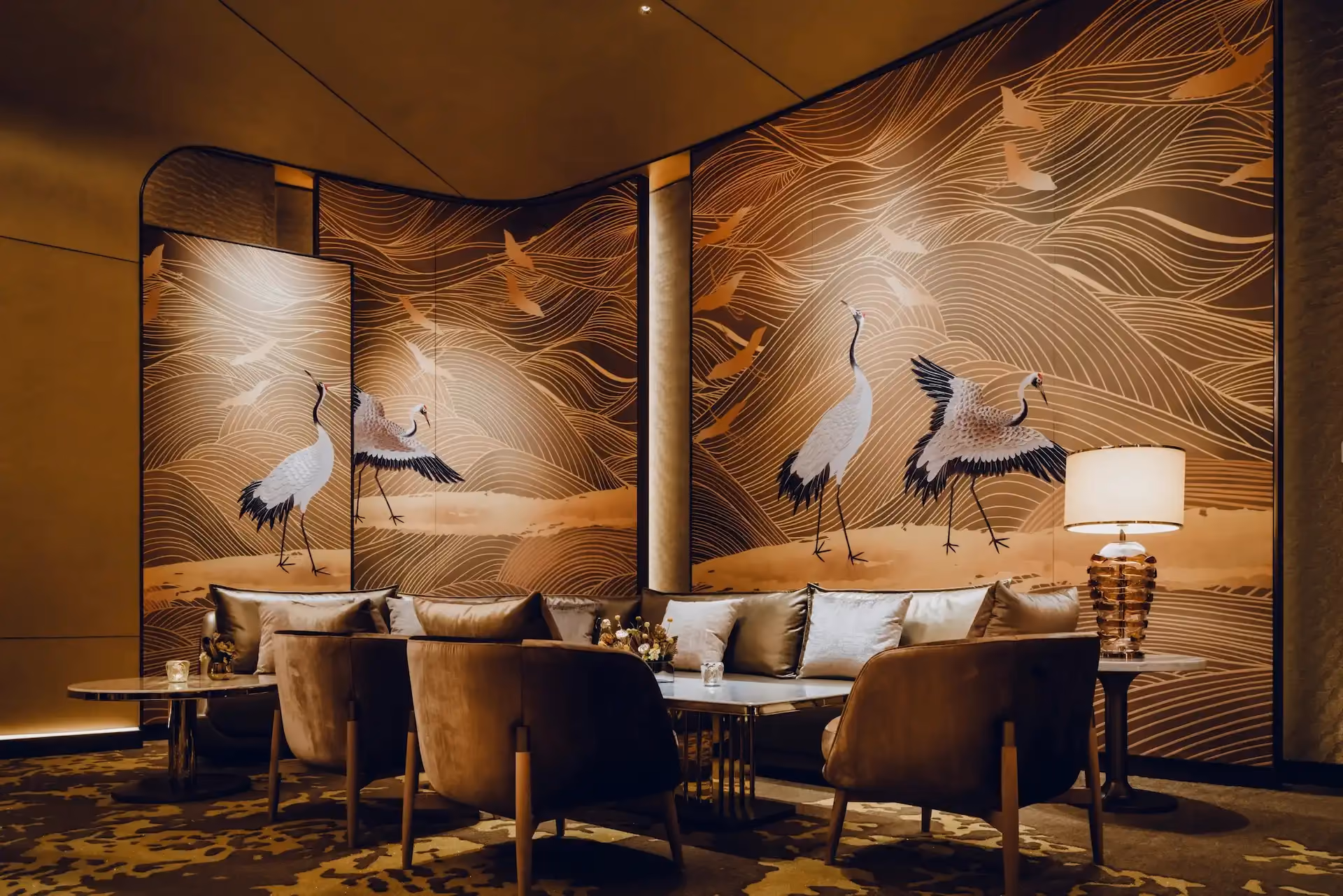 Grand Imperial Court lounge seating area at MGM Macao featuring gold crane mural panels with flowing wave line motifs, curved upholstered banquette seating, marble coffee tables and layered ambient lighting within a luxury Chinese restaurant private dining environment