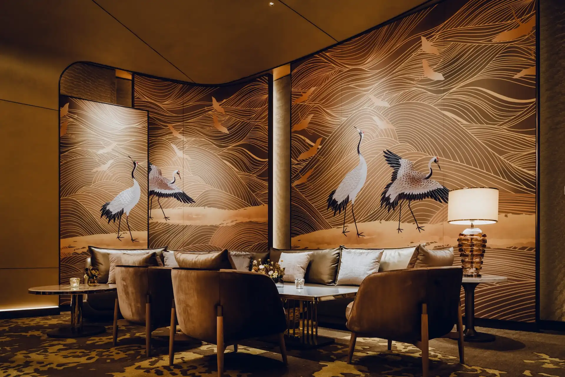 Grand Imperial Court lounge seating area at MGM Macao featuring gold crane mural panels with flowing wave line motifs, curved upholstered banquette seating, marble coffee tables and layered ambient lighting within a luxury Chinese restaurant private dining environment