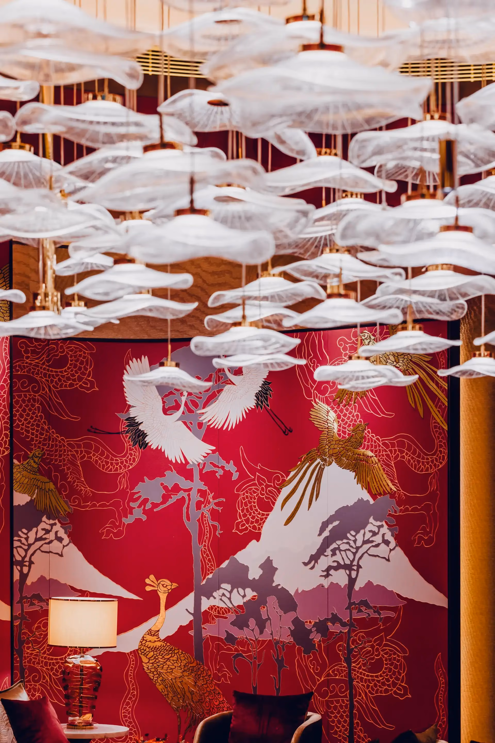 Grand Imperial Court Tapestry Of Parchment private dining interior at MGM Macao featuring suspended layered glass pendant installation above red lacquer wall panels with gold and white phoenix murals, mountain landscape motifs and bespoke luxury Chinese restaurant detailing