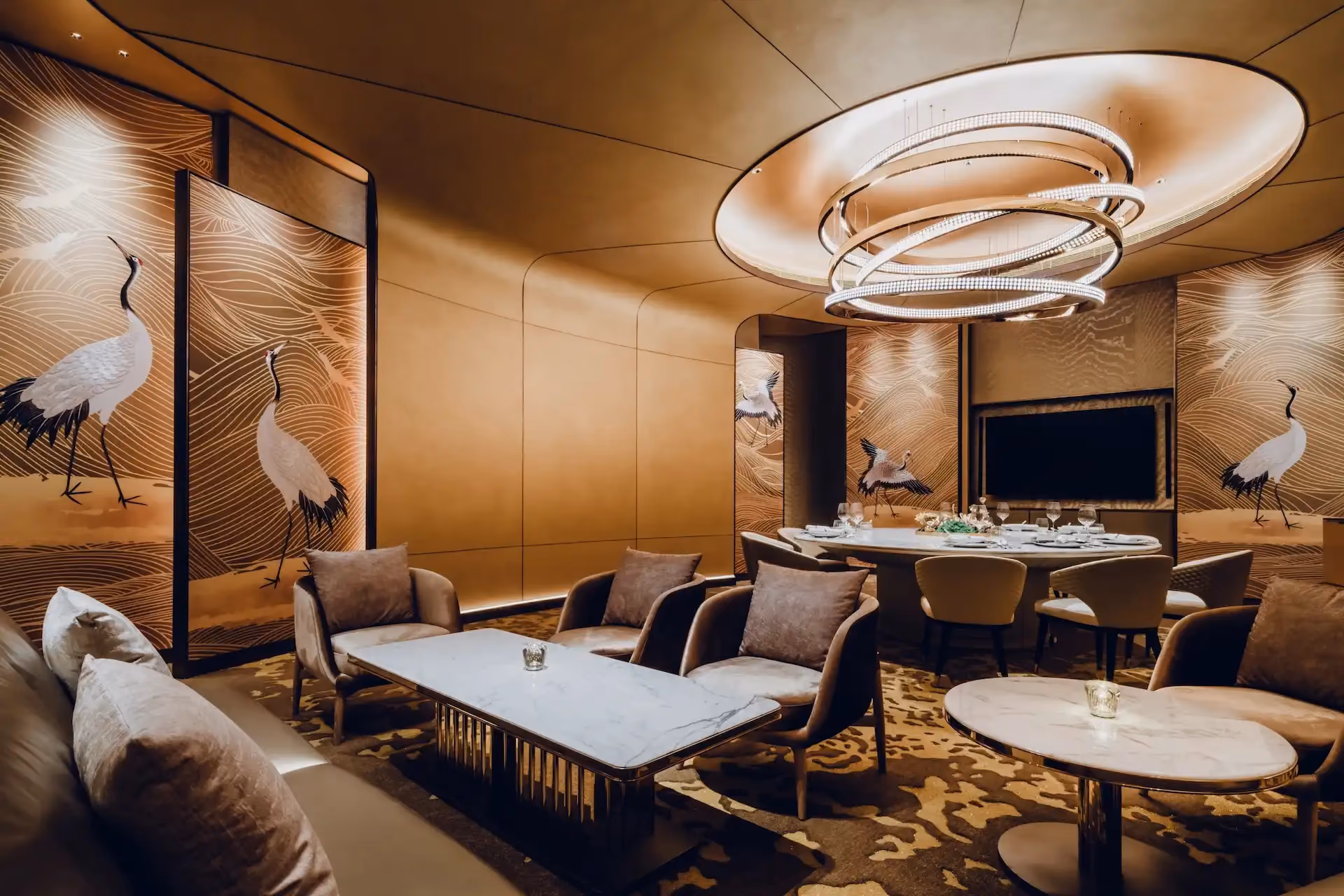 Grand Imperial Court private dining room at MGM Macao featuring gold crane wall panels with flowing line motifs, bespoke circular chandelier within recessed ceiling, marble dining table and upholstered lounge seating in a luxury Chinese restaurant interior design