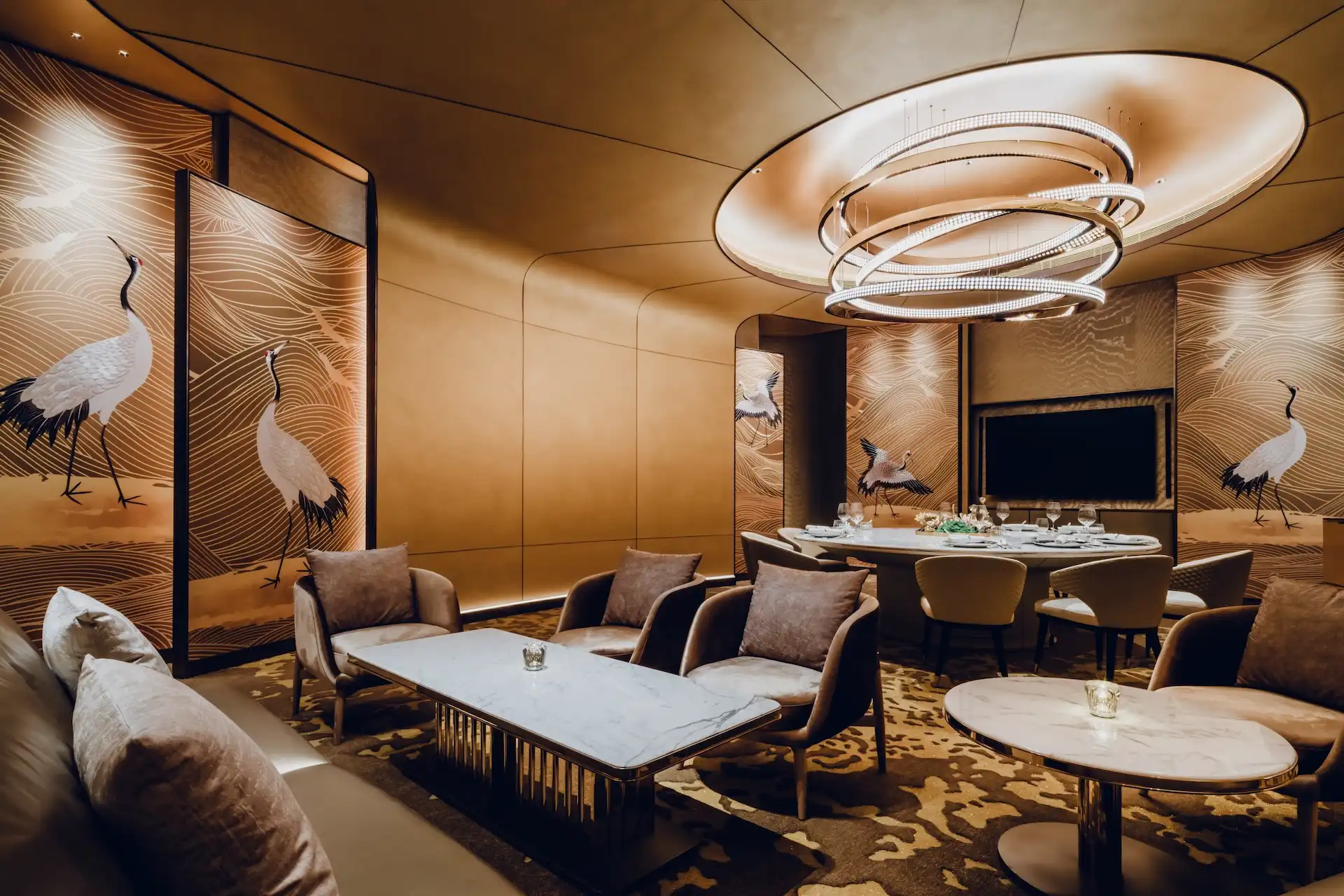 Grand Imperial Court private dining room at MGM Macao featuring gold crane wall panels with flowing line motifs, bespoke circular chandelier within recessed ceiling, marble dining table and upholstered lounge seating in a luxury Chinese restaurant interior design