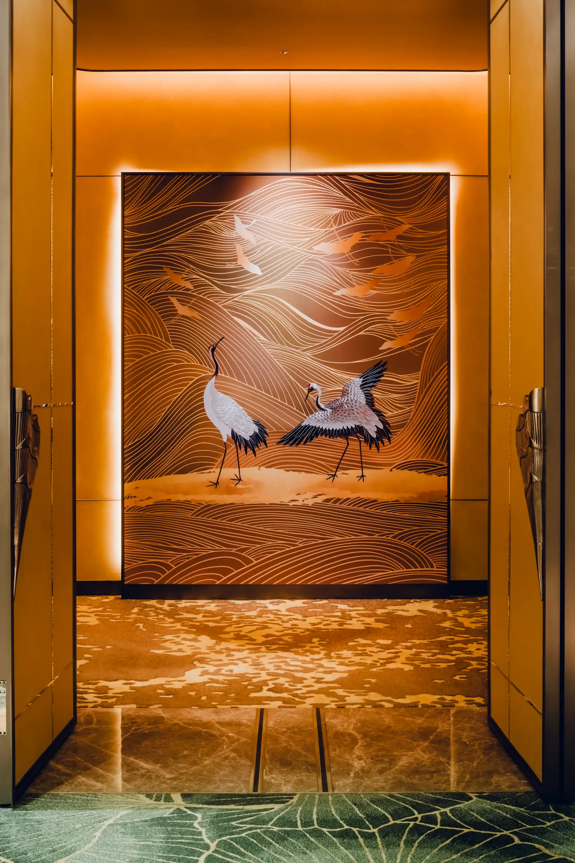 Grand Imperial Court entrance feature panel at MGM Macao showcasing illuminated gold crane artwork with flowing line motifs and layered landscape pattern framed by bespoke gold doors, forming a ceremonial threshold within a luxury Chinese restaurant interior