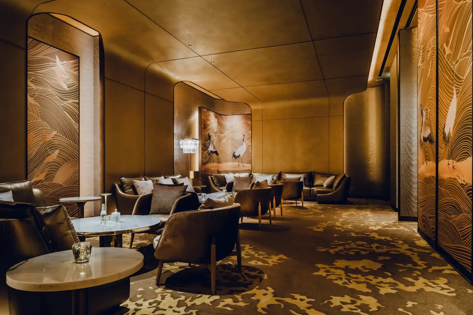 Grand Imperial Court lounge corridor seating area at MGM Macao featuring gold crane mural panels with flowing wave motifs, curved wall geometry, marble side tables and upholstered armchairs arranged within a softly illuminated luxury Chinese restaurant interior