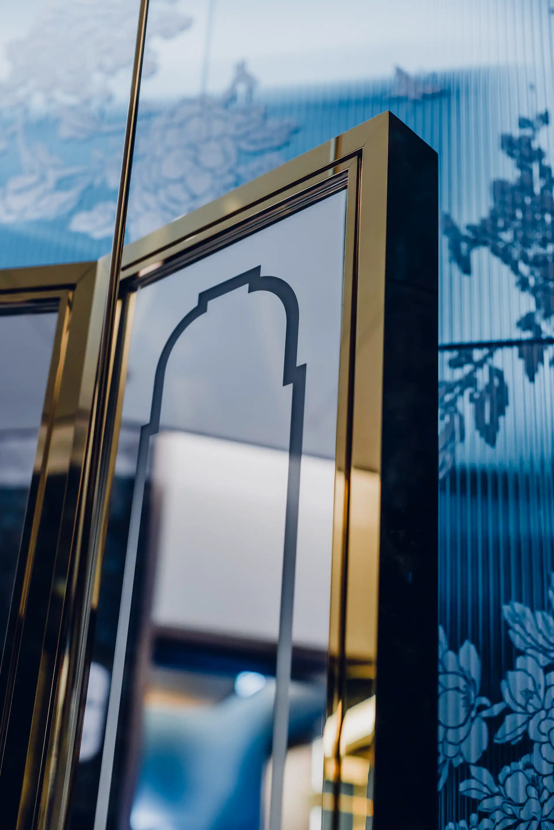Mirror detail in Tapestry of Butterfly Wings restroom at Grand Imperial Court MGM Macau featuring brass framed mirror panels and blue patterned glass backdrop with floral motifs.