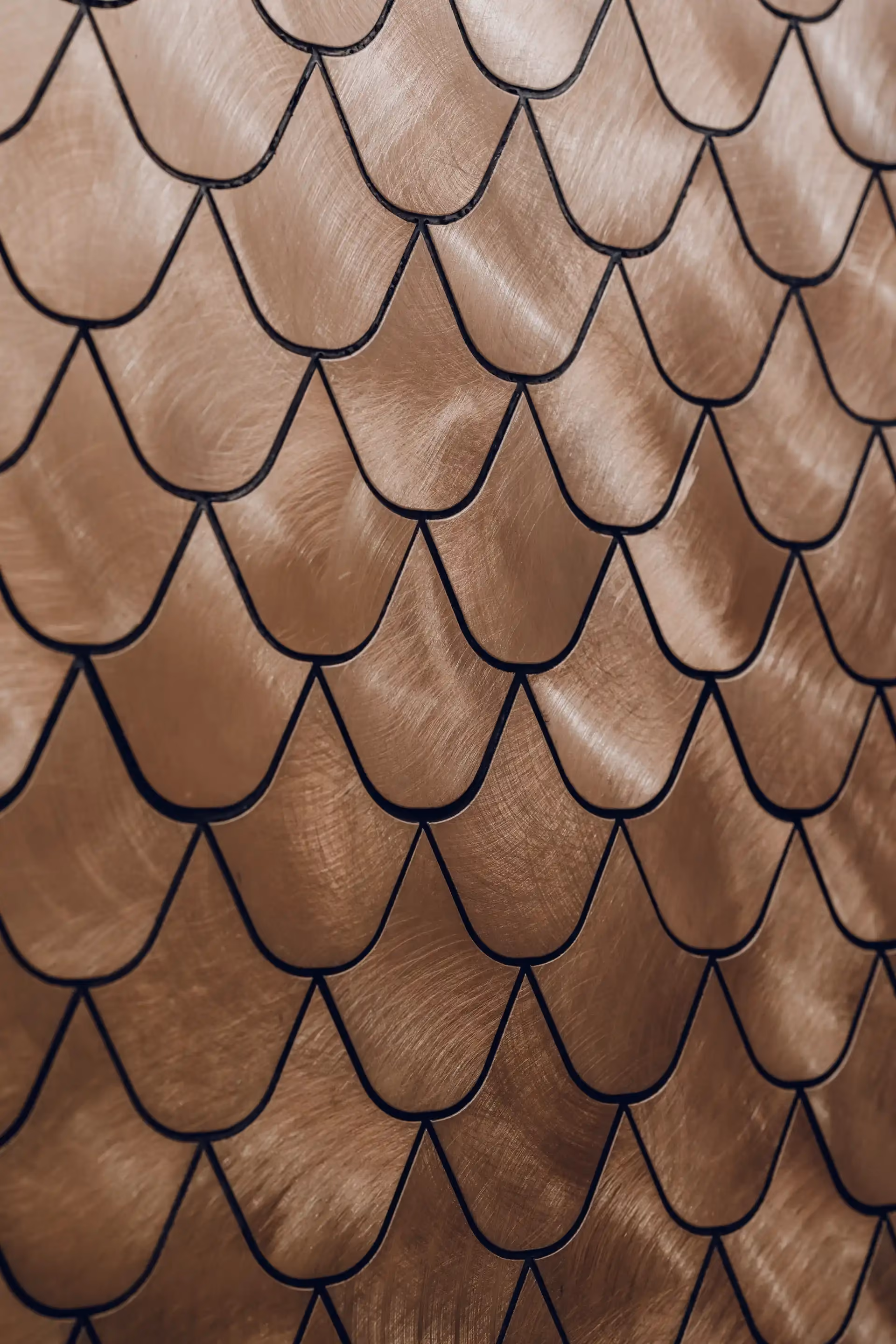 Close up of metallic gold scalloped wall tiles forming a layered leaf pattern with brushed texture and dark grout lines.