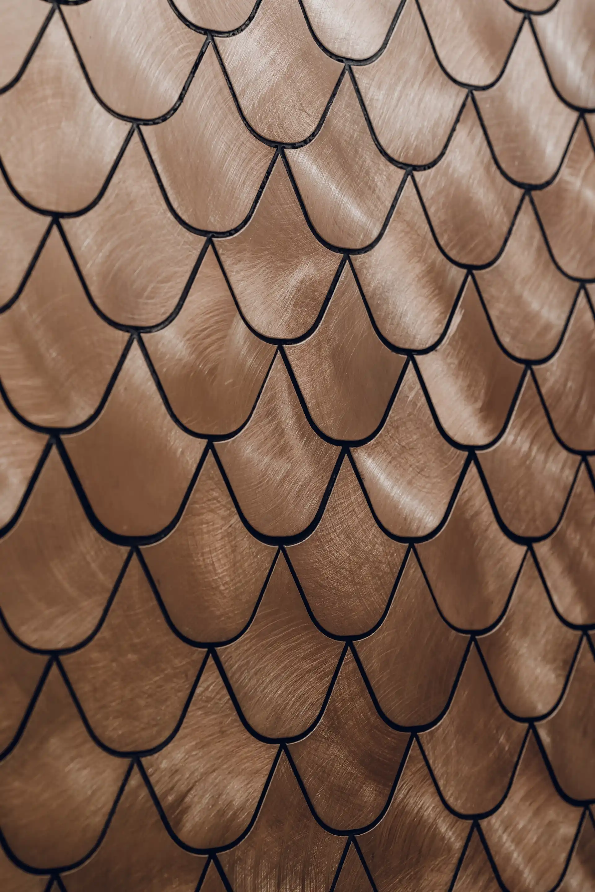 Close up of metallic gold scalloped wall tiles forming a layered leaf pattern with brushed texture and dark grout lines.