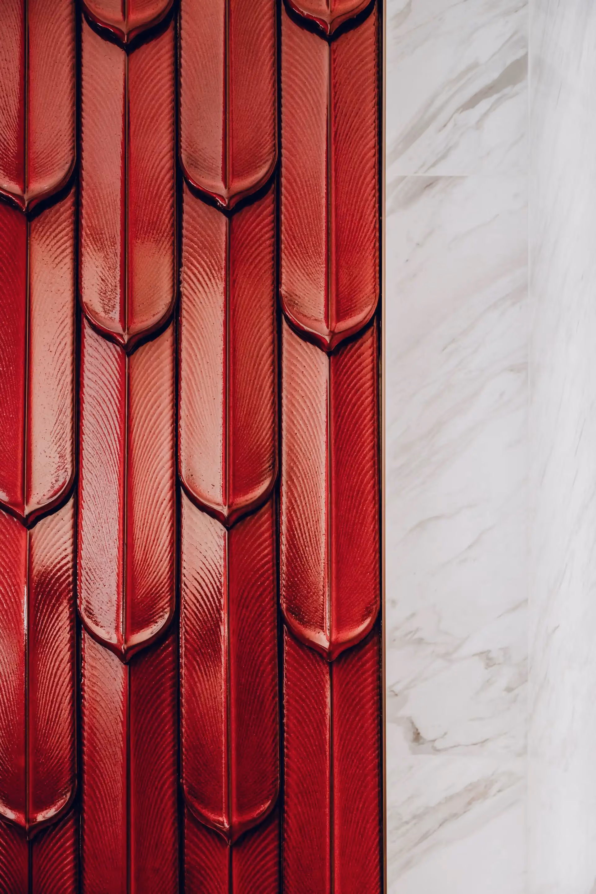 Close up of deep red vertically laid ceramic wall tiles with sculpted feather like relief and glossy finish in Tapestry of Parchment restroom.