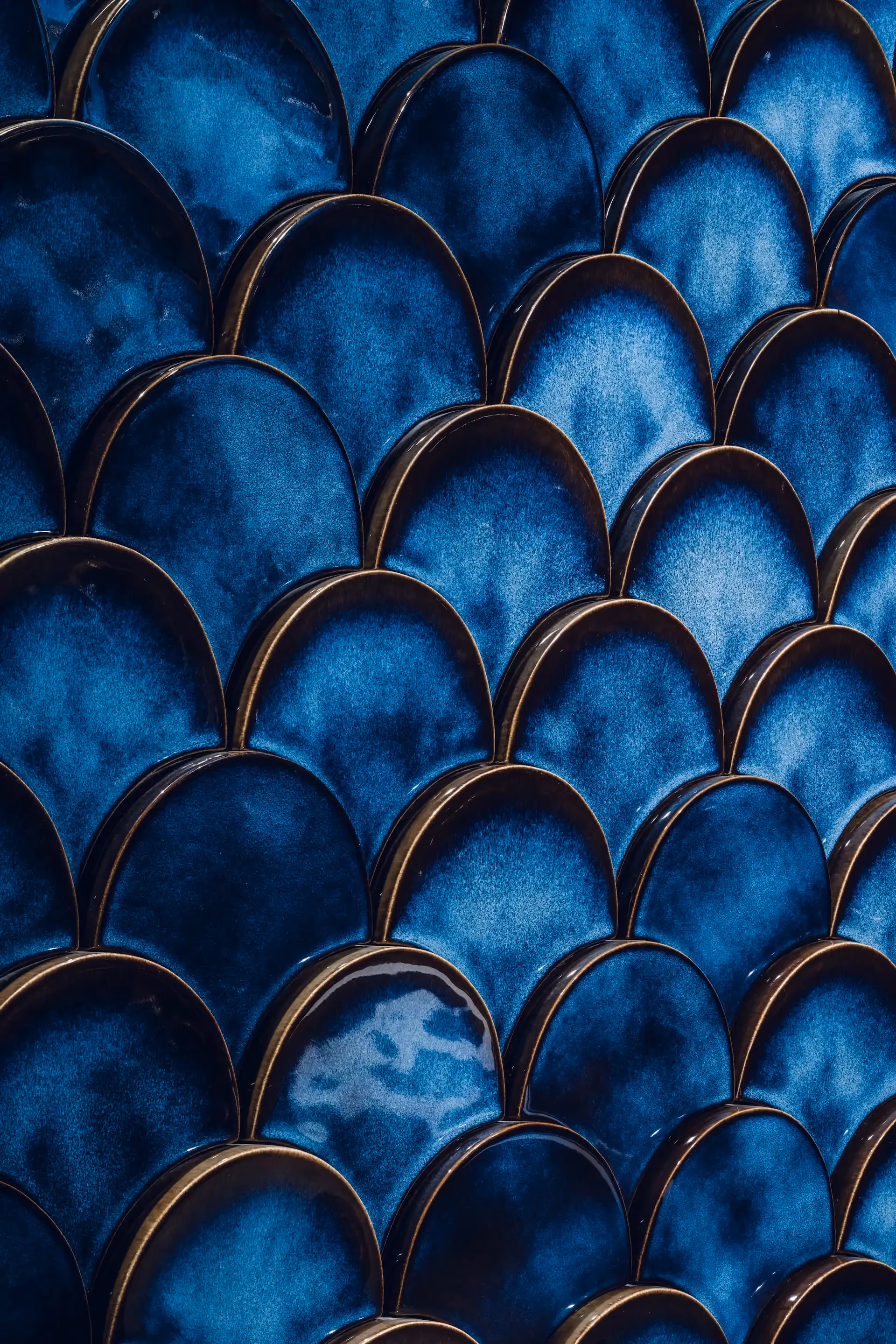 Close up of deep blue scalloped ceramic wall tiles with glossy finish forming a layered butterfly wing pattern.