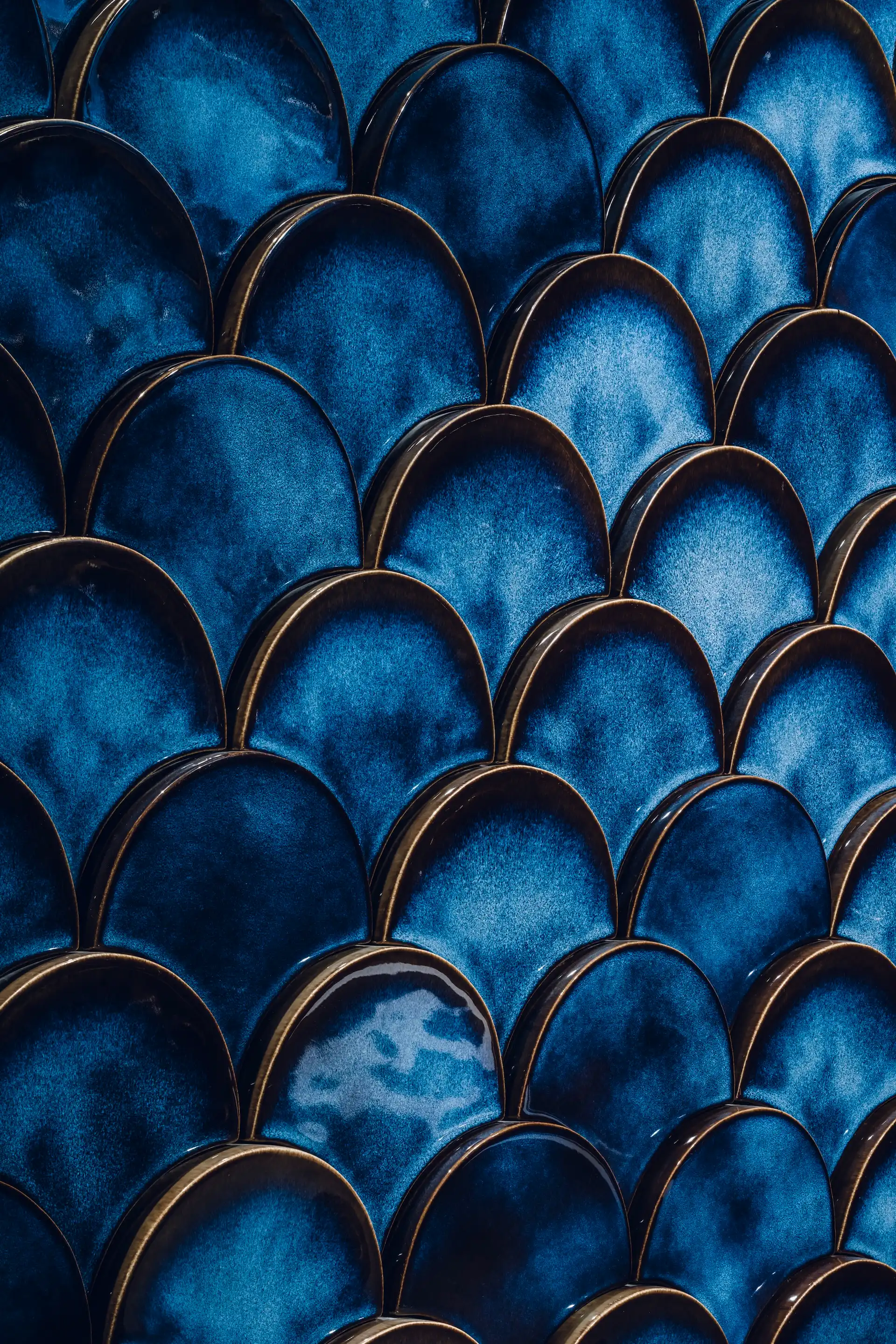 Close up of deep blue scalloped ceramic wall tiles with glossy finish forming a layered butterfly wing pattern.