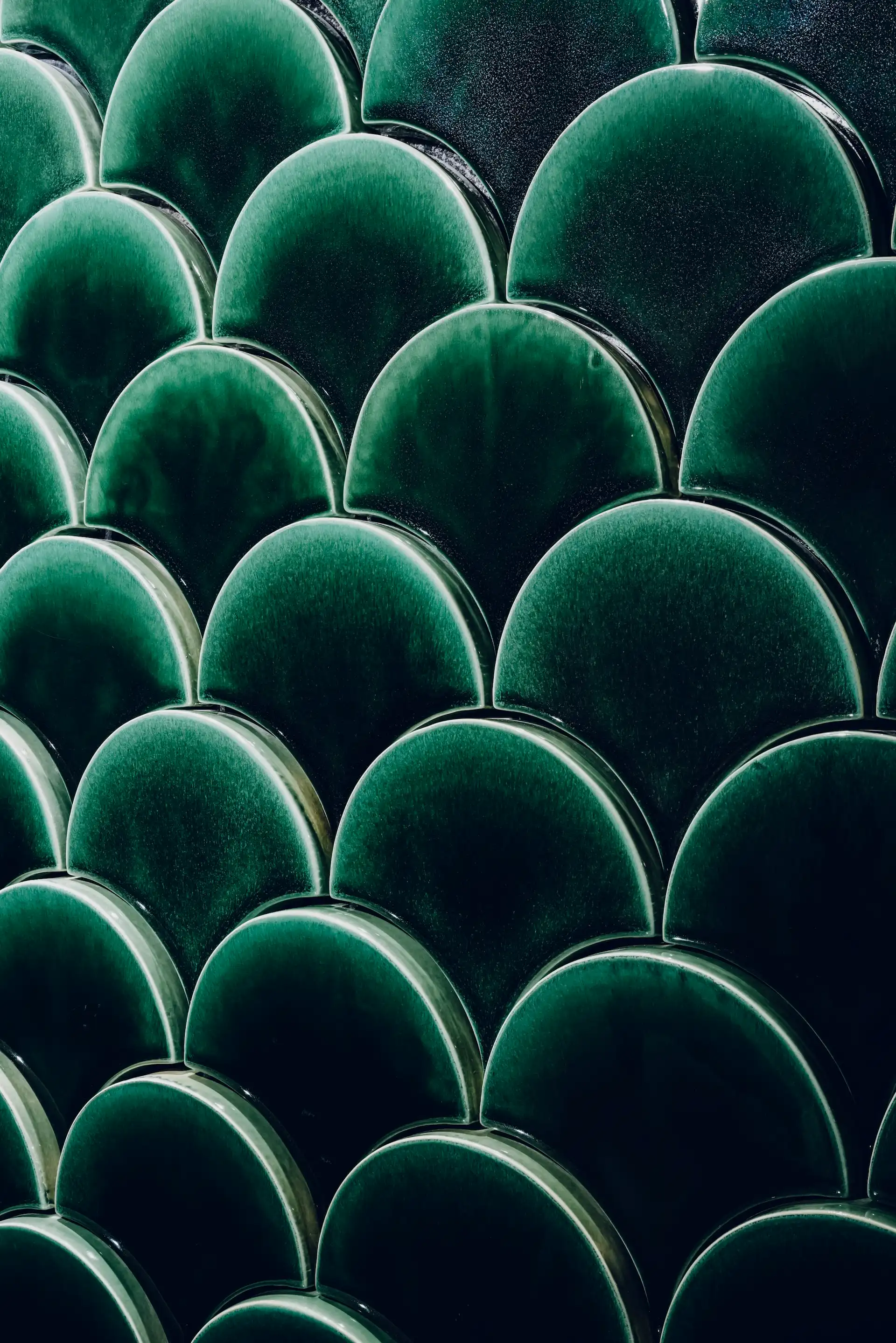 Close up of deep green scalloped ceramic wall tiles in Tapestry of Feathers restroom at Grand Imperial Court MGM Macau with glossy finish and layered feather inspired pattern.