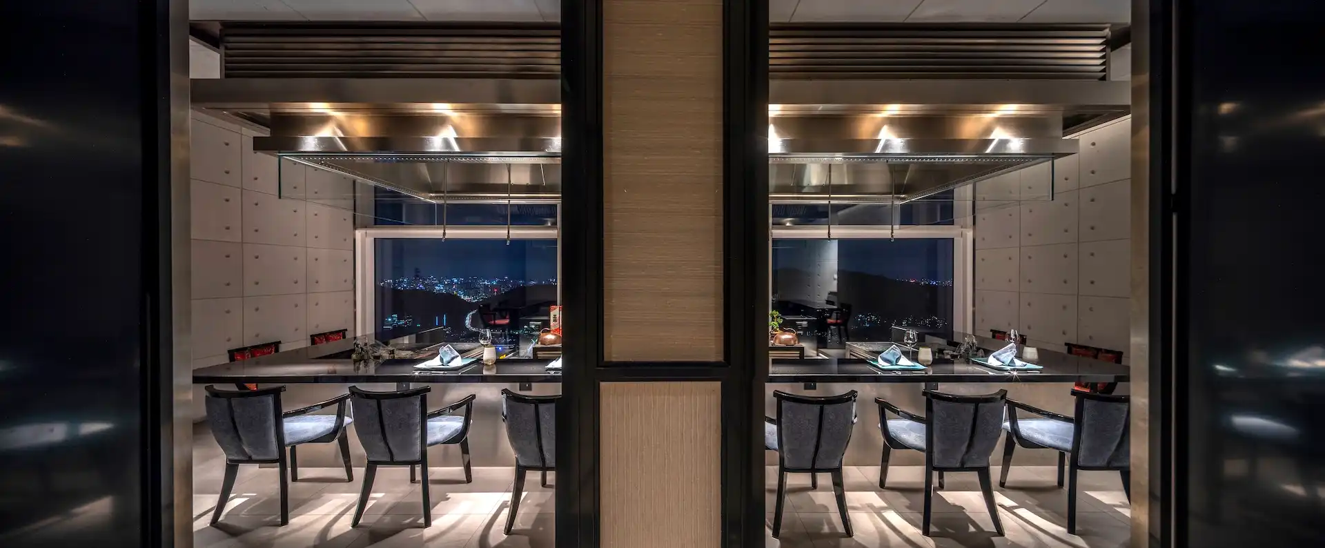 Concrete Room private teppanyaki dining space at RIN Mandarin Oriental Shenzhen featuring exposed concrete wall panels with recessed detailing, a central granite chef counter beneath a suspended stainless steel extraction hood, and panoramic night views of the Shenzhen skyline framed by floor to ceiling glazing.