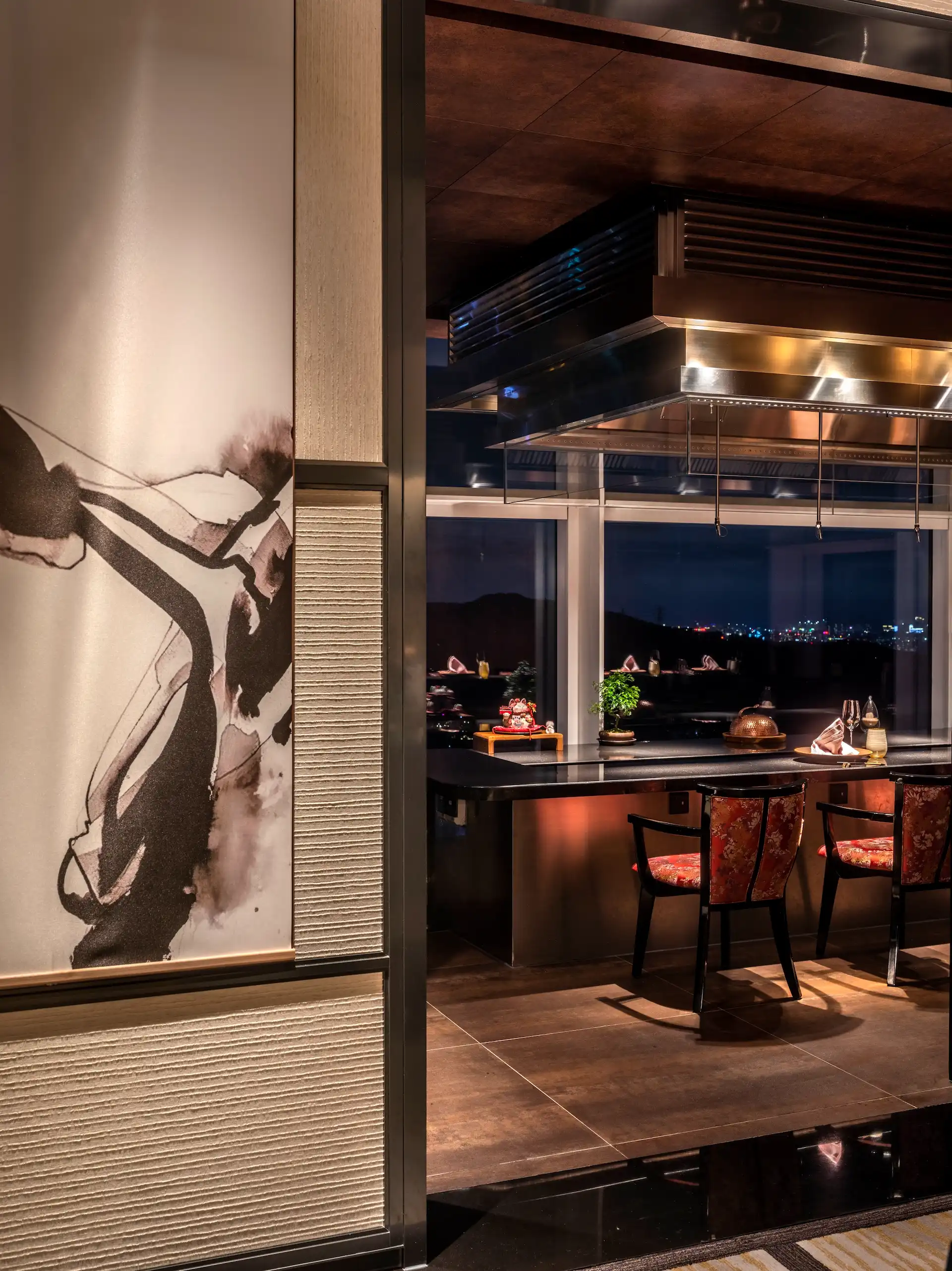View from the sake lounge into a private dining room at RIN Mandarin Oriental Shenzhen featuring corten steel wall cladding, open counter seating, Japanese ink artwork panel and floor to ceiling windows overlooking the city at night.