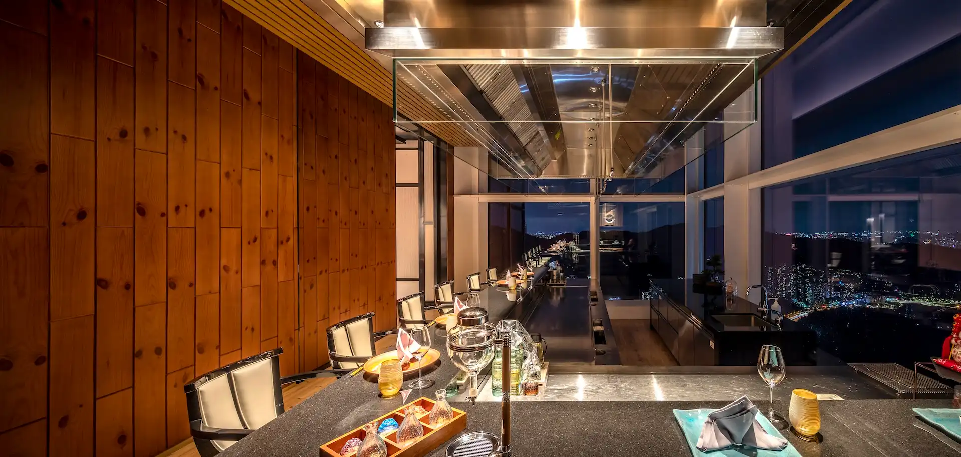 Pine Room teppanyaki counter at RIN Mandarin Oriental Shenzhen featuring a long granite chef station, suspended stainless steel extraction hood, pine timber wall paneling, and floor to ceiling windows overlooking the Shenzhen night skyline.