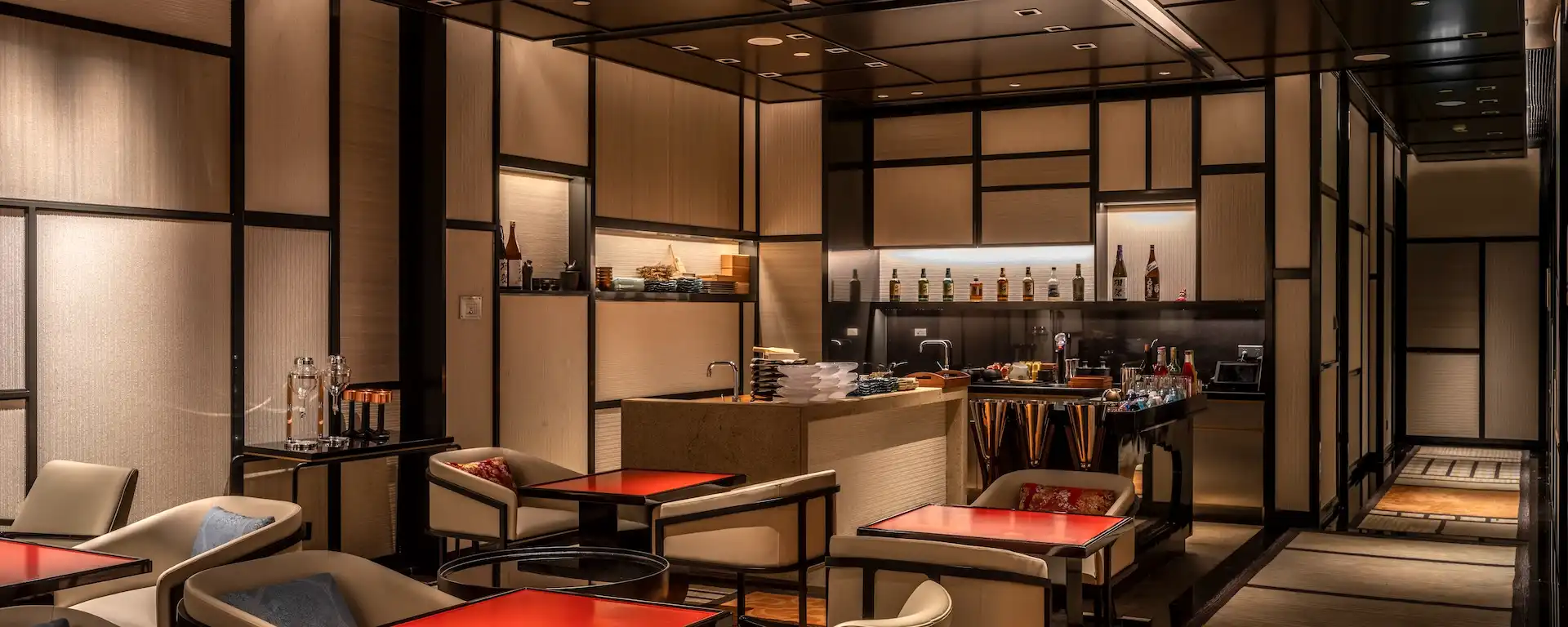 Sake lounge at RIN Mandarin Oriental Shenzhen featuring intimate seating, red lacquer table tops, Japanese inspired wall paneling, back bar display with premium sake bottles and open preparation counter within a refined contemporary setting.