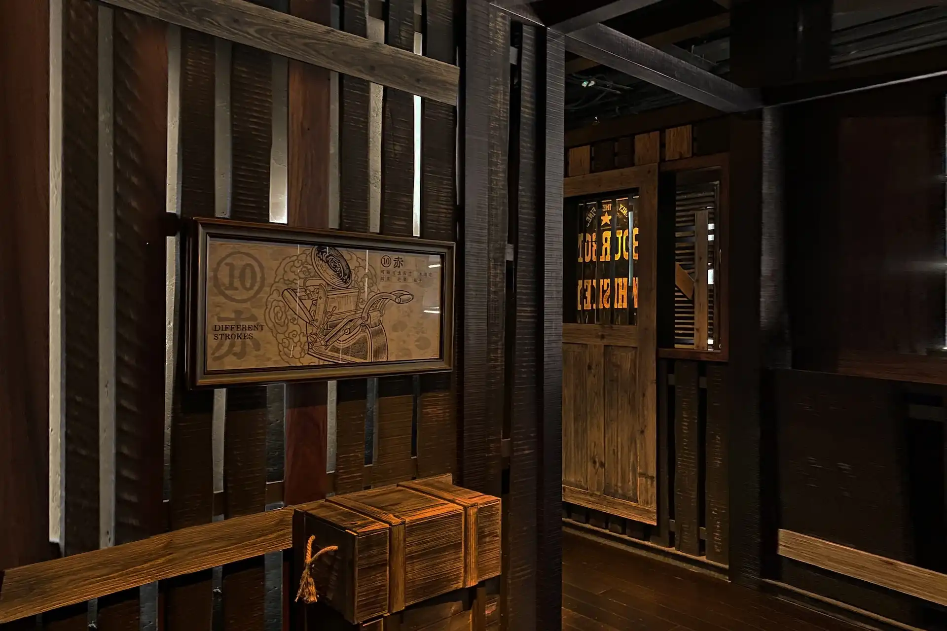 Entrance to Prohibition Bar at Mandarin Oriental Shenzhen featuring dark timber slatted wall panels, vintage framed illustration artwork, concealed wooden door with illuminated signage, and a speakeasy inspired interior atmosphere.