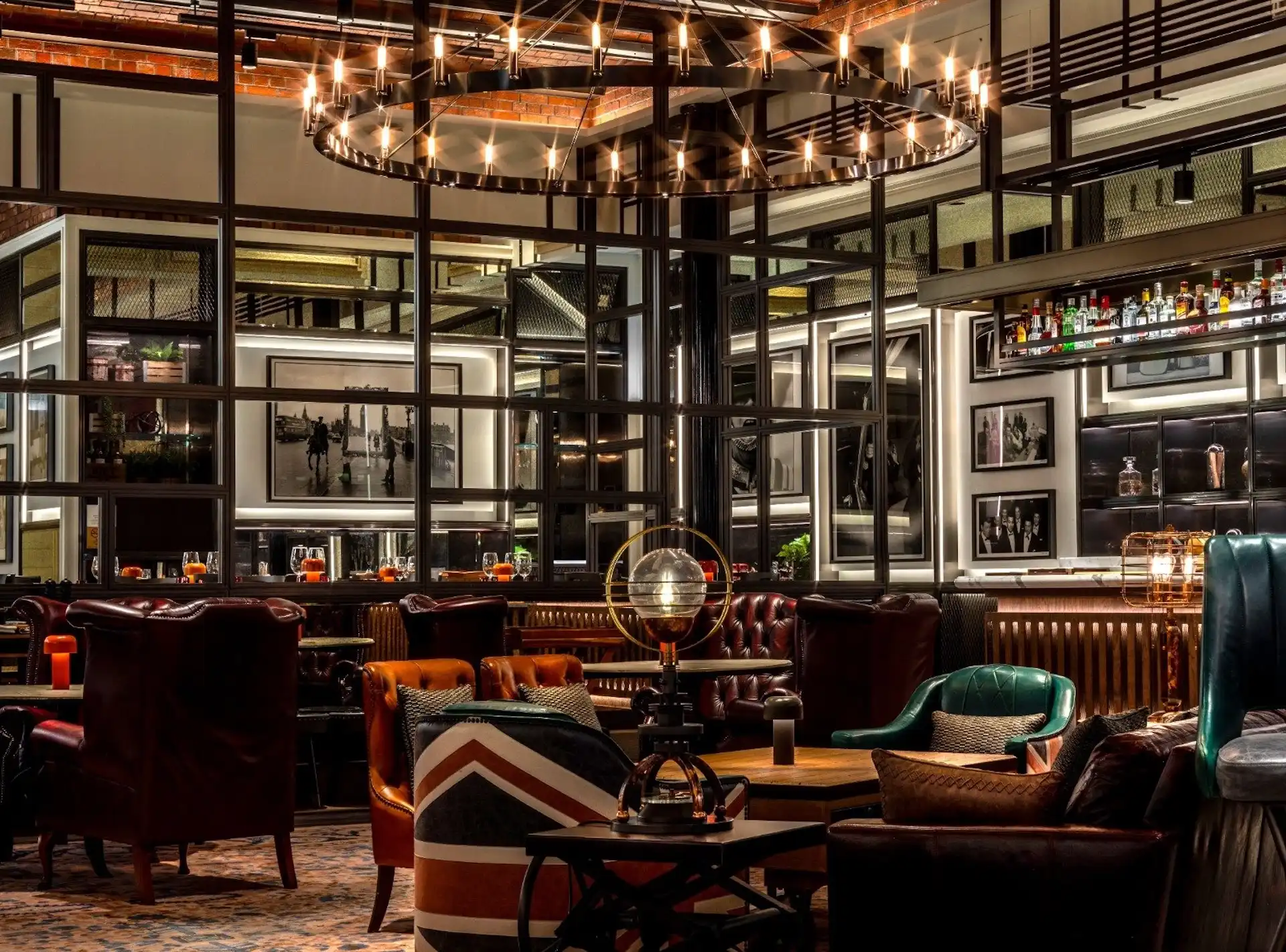 Lounge seating area at Gordon Ramsay Pub & Grill at The Londoner Macao featuring leather armchairs, Union Jack accent chair, timber tables, framed black and white photography, and a circular chandelier above within a contemporary British pub interior.