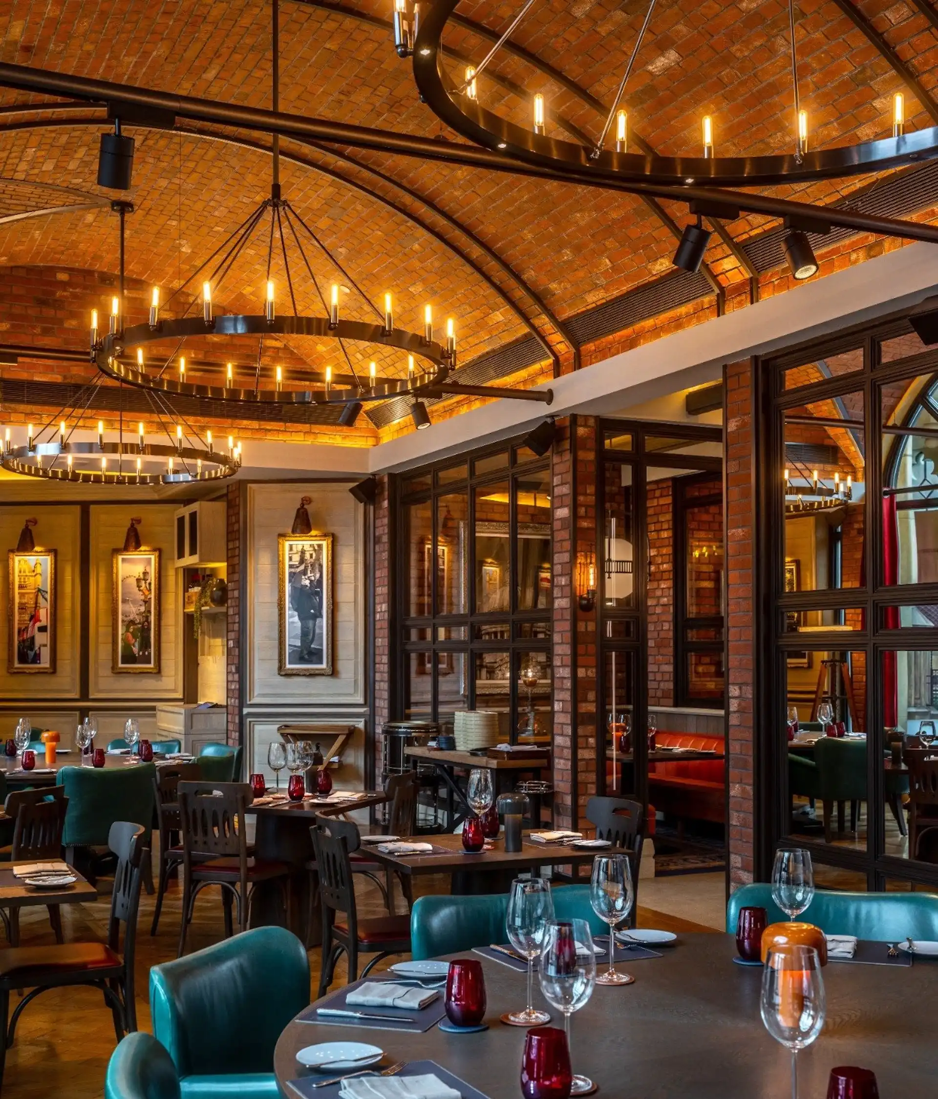 Dining interior at Gordon Ramsay Pub & Grill at The Londoner Macao featuring brick vaulted ceilings, circular ring chandeliers, timber dining tables set with red glassware, green leather chairs, and framed artwork within a British pub inspired restaurant setting.