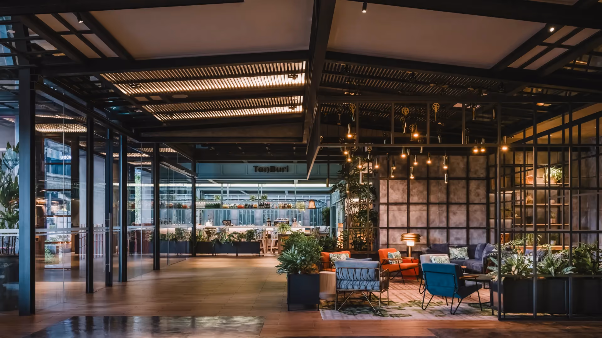Lobby lounge at Hyatt Centric City Centre Kuala Lumpur, with steel-framed structures, pendant lights, orange and teal armchairs and planting