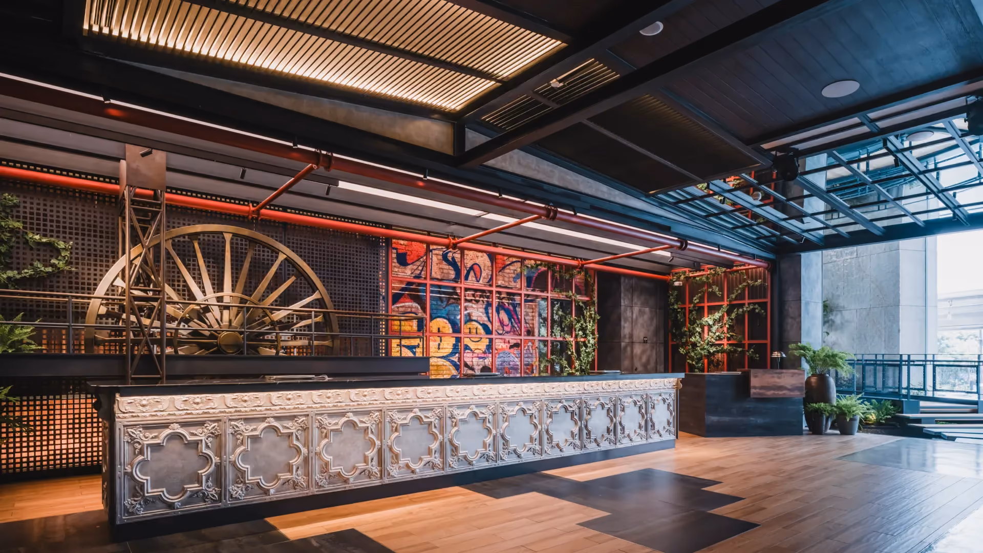 Main reception at Hyatt Centric City Centre Kuala Lumpur, with a pressed tin counter, a tin dredger gear wheel and illuminated mesh screens over street art