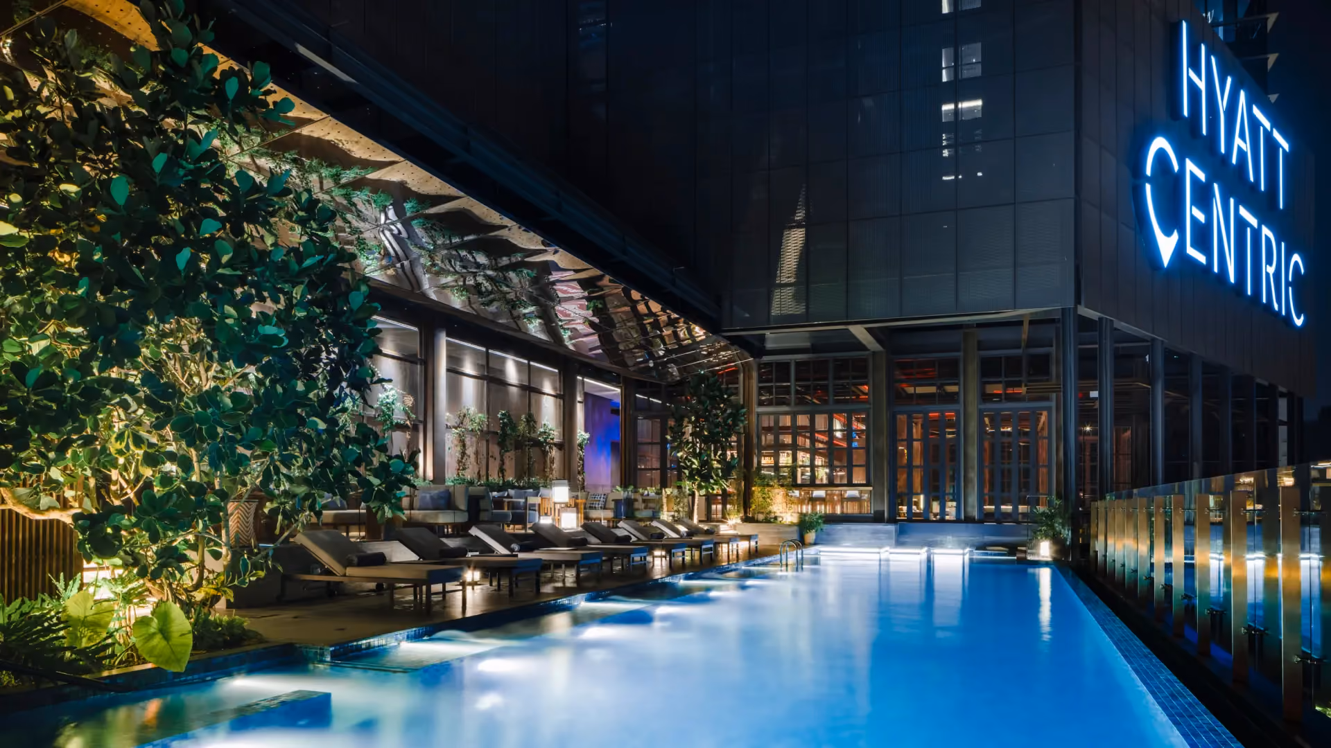 @21 pool at Hyatt Centric City Centre Kuala Lumpur at night, with loungers, a planted wall and the illuminated Hyatt Centric sign