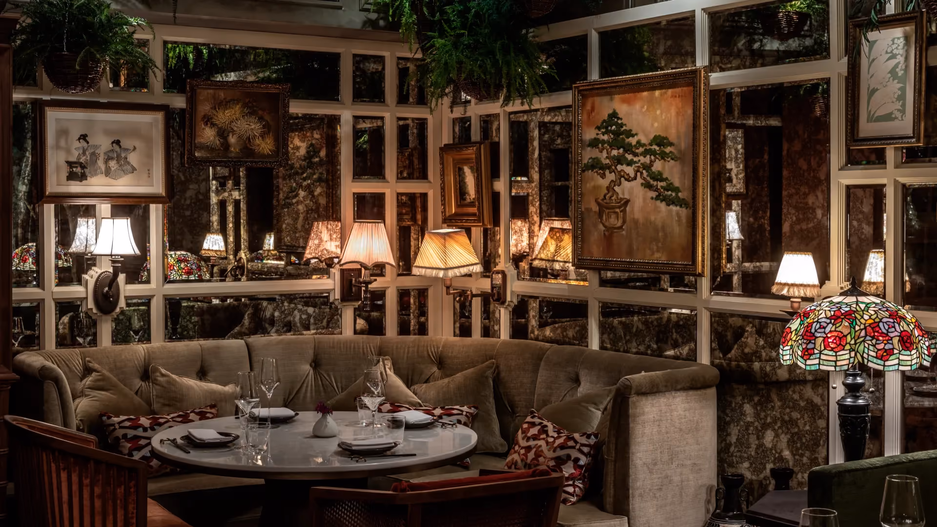 Curio Lounge at The Aubrey, Mandarin Oriental Hong Kong, with a curved banquette, framed botanical artworks, table lamps and greenery