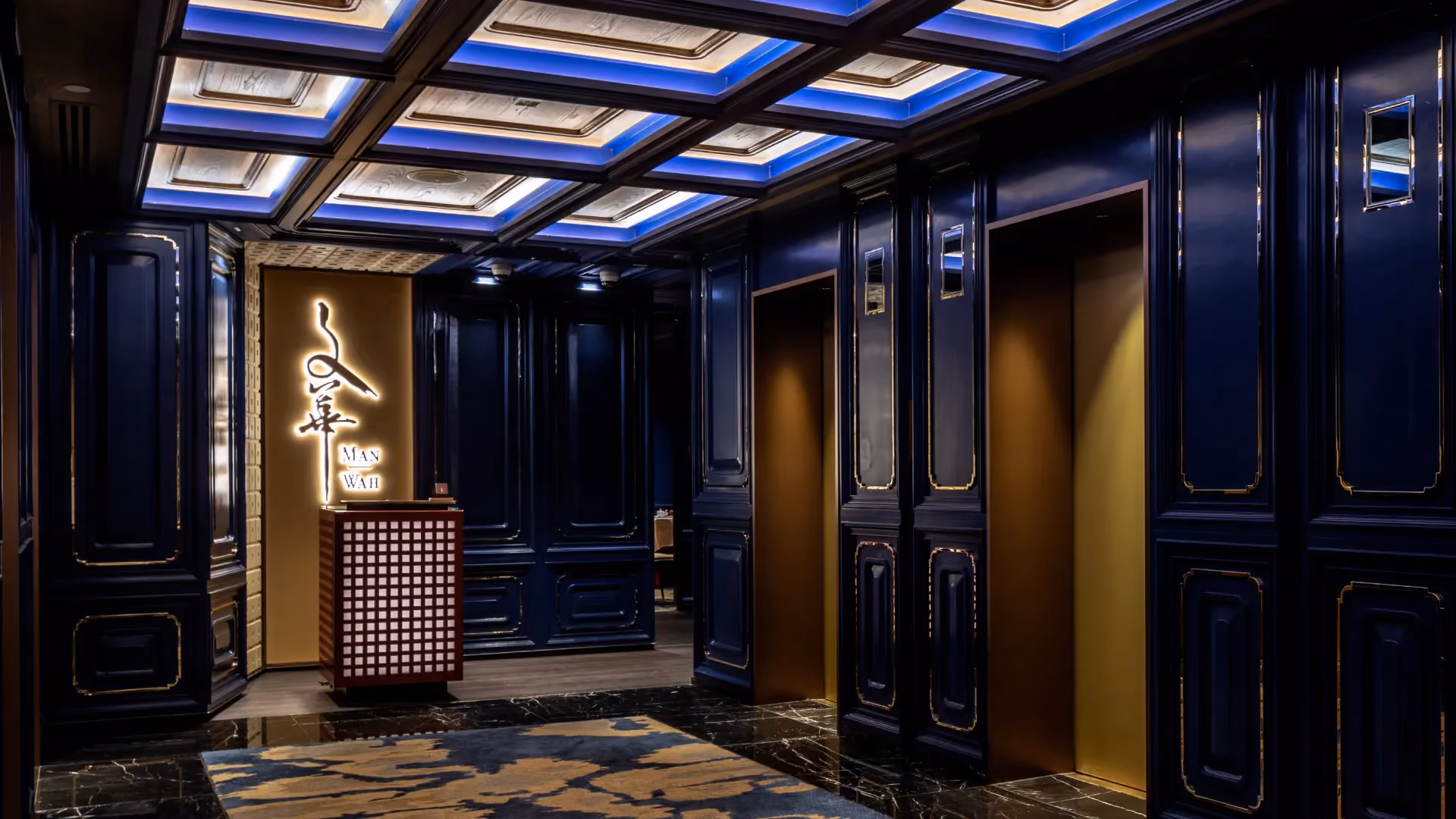 Lift lobby at Man Wah, Mandarin Oriental Hong Kong, with deep blue lacquered timber panels, brass inlay detail and a coffered ceiling
