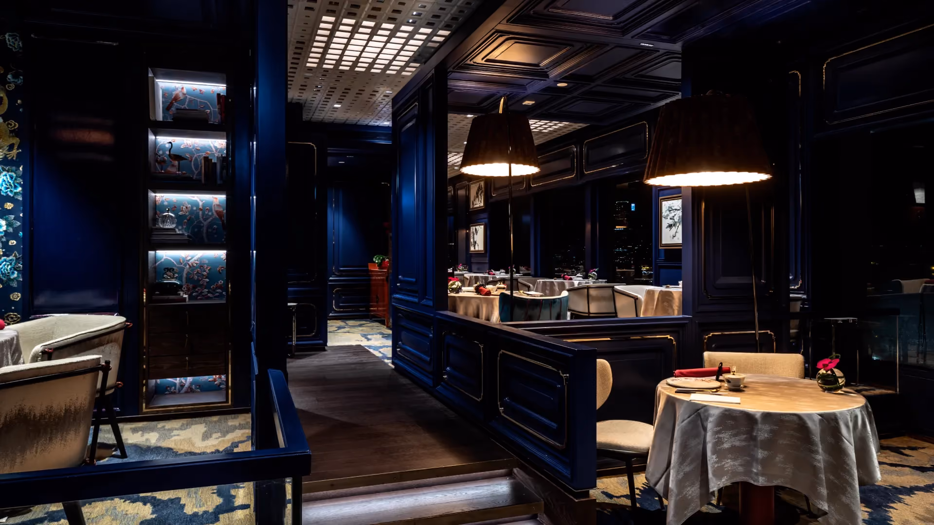 Main dining room at Man Wah, Mandarin Oriental Hong Kong, with raised dining platforms, blue lacquered panelling, pendant lamps and a grid fretwork ceiling