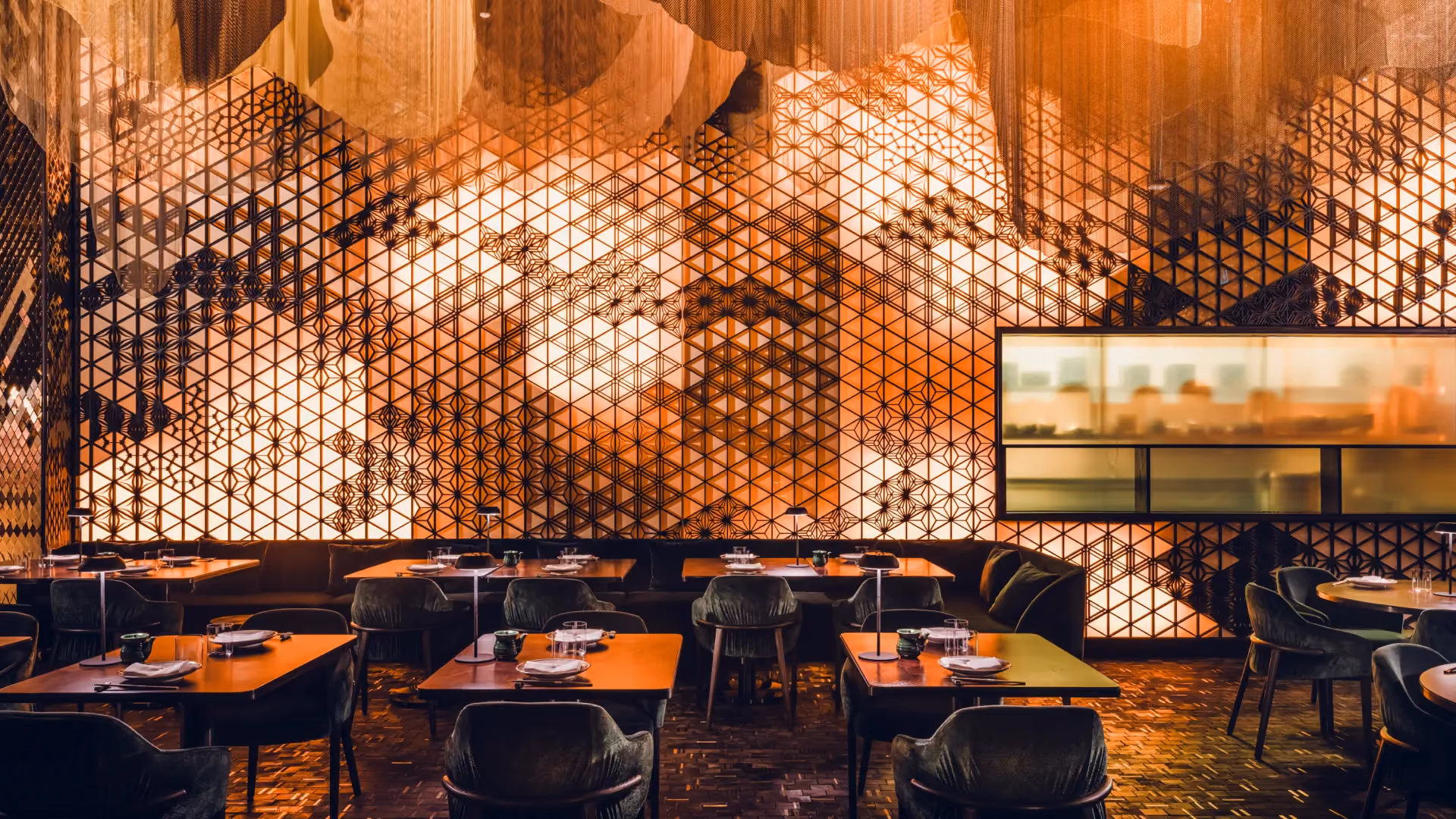 Back-illuminated Kumiko screen wall in the main dining room at Strawfire, Emirates Palace Abu Dhabi, with draped ceiling and emerald chairs